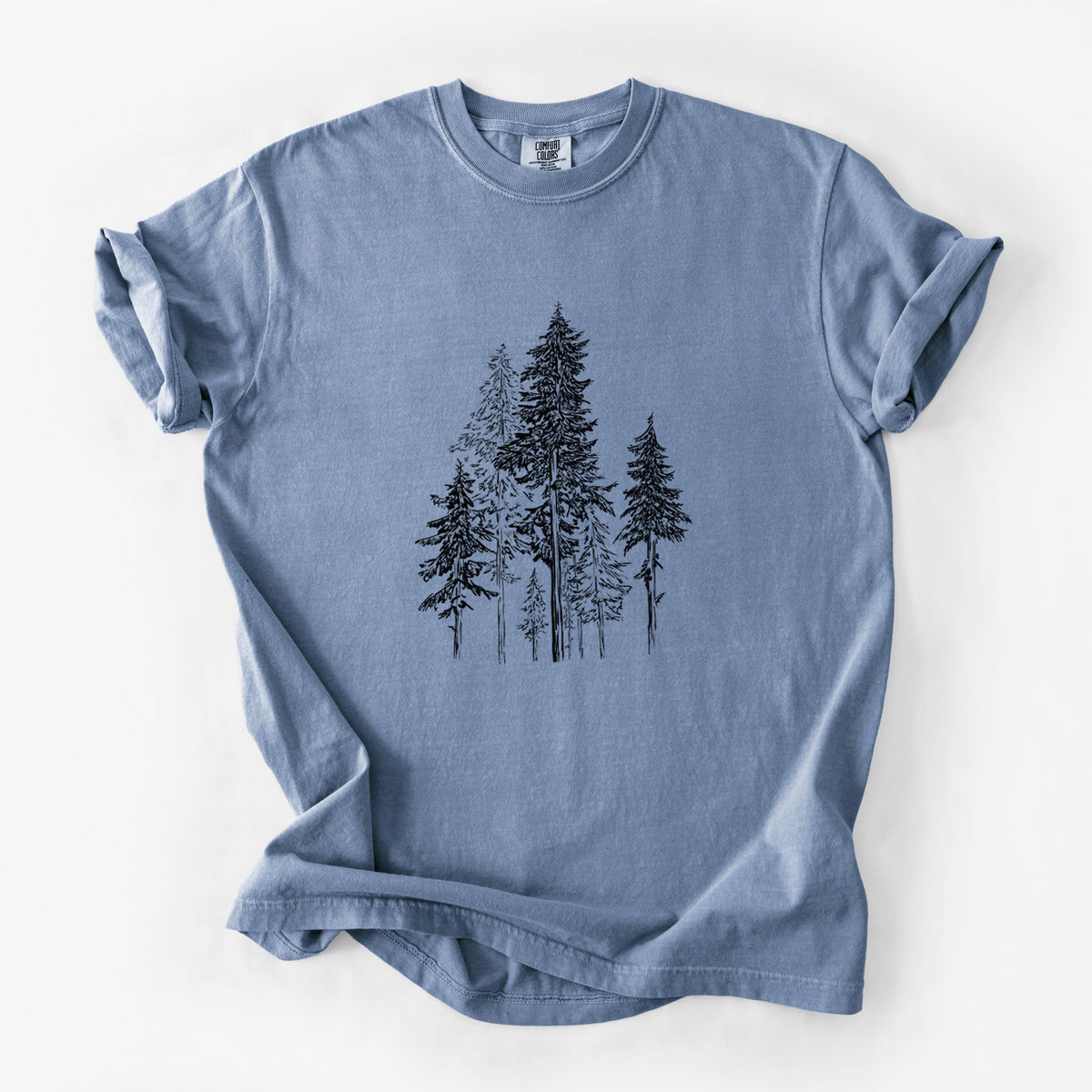 Blue jean Comfort Colors t-shirt laid flat, printed with a black ink illustration of a forest of tall hemlock trees.
