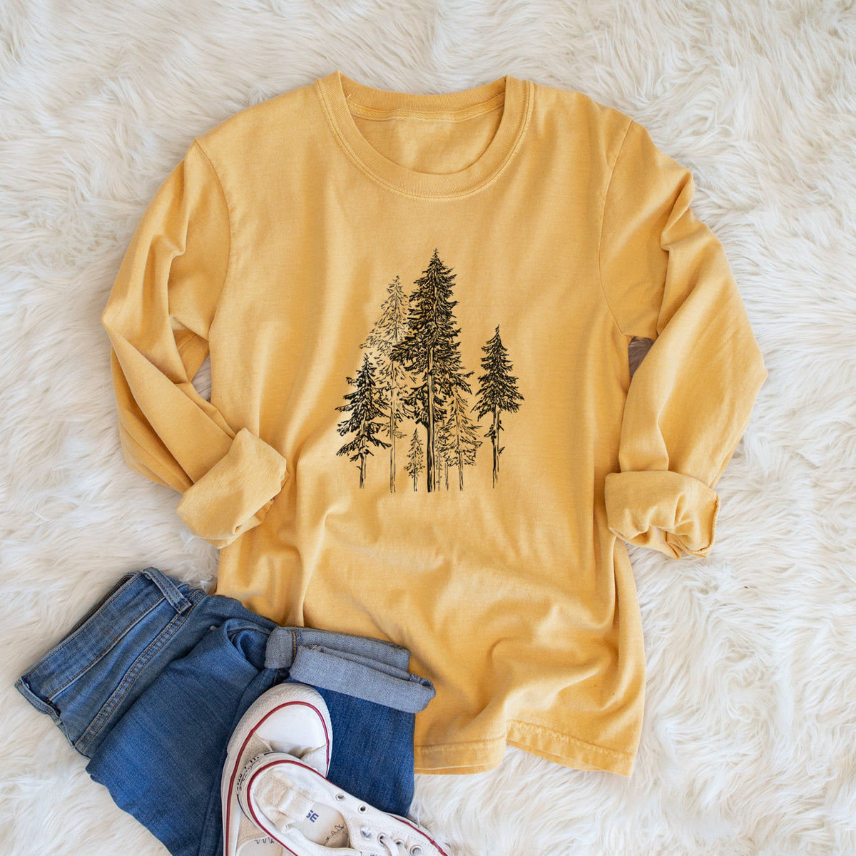 Golden wheat yellow Comfort Colors long sleeve shirt printed with a black ink illustration of a forest of tall hemlock trees, shown in a lifestyle photo.