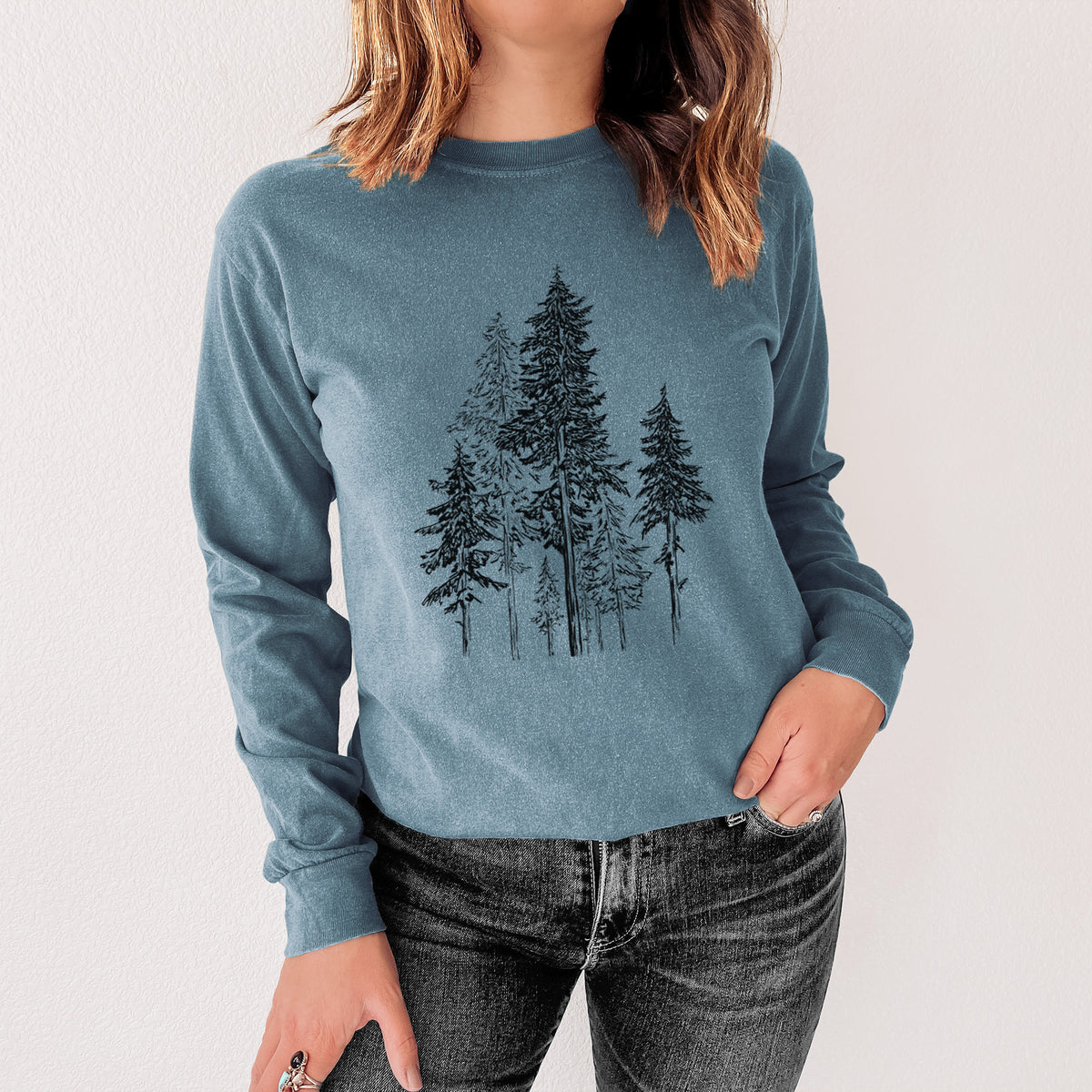Steel blue Comfort Colors long sleeve shirt printed with a black ink illustration of a forest of tall hemlock trees, shown in a lifestyle photo.
