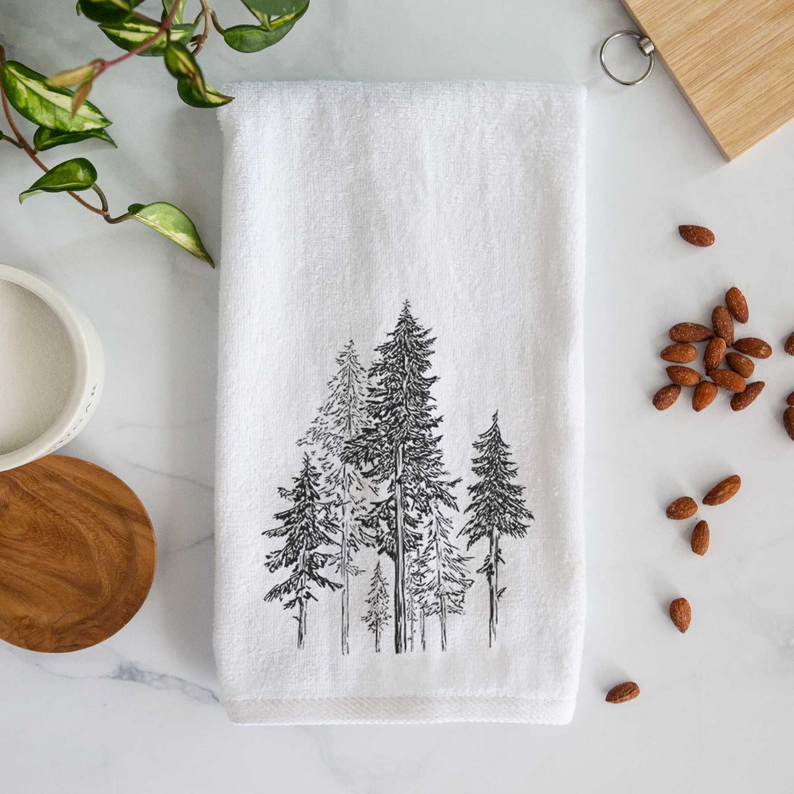 White hand towel printed with a black ink illustration of a forest of tall hemlock trees.