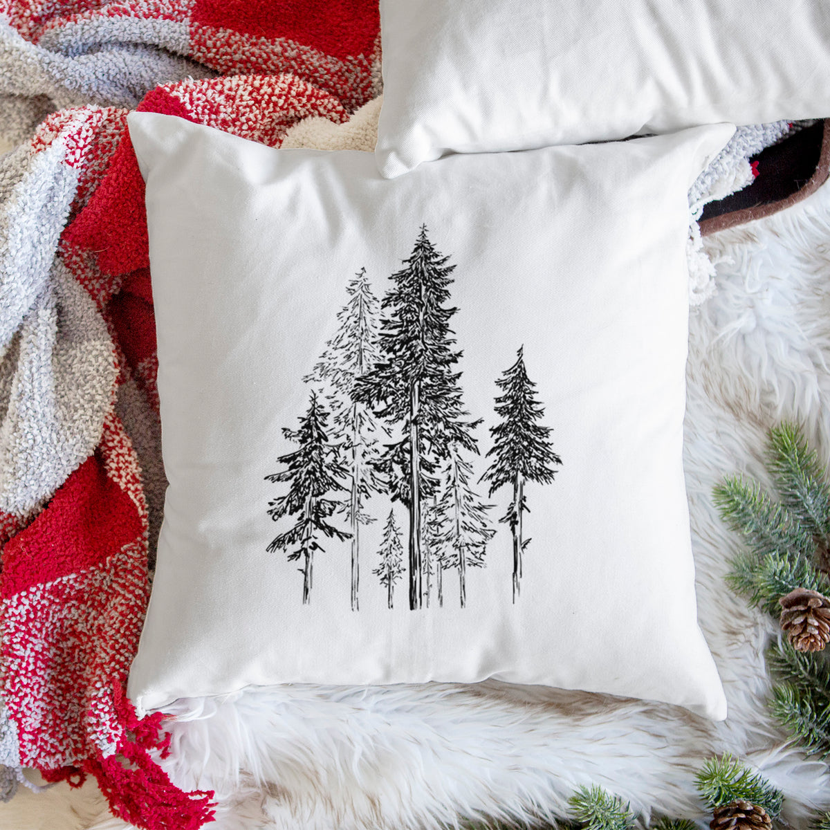 White pillow cover printed with a black ink illustration of a forest of tall hemlock trees, on a woven chair.