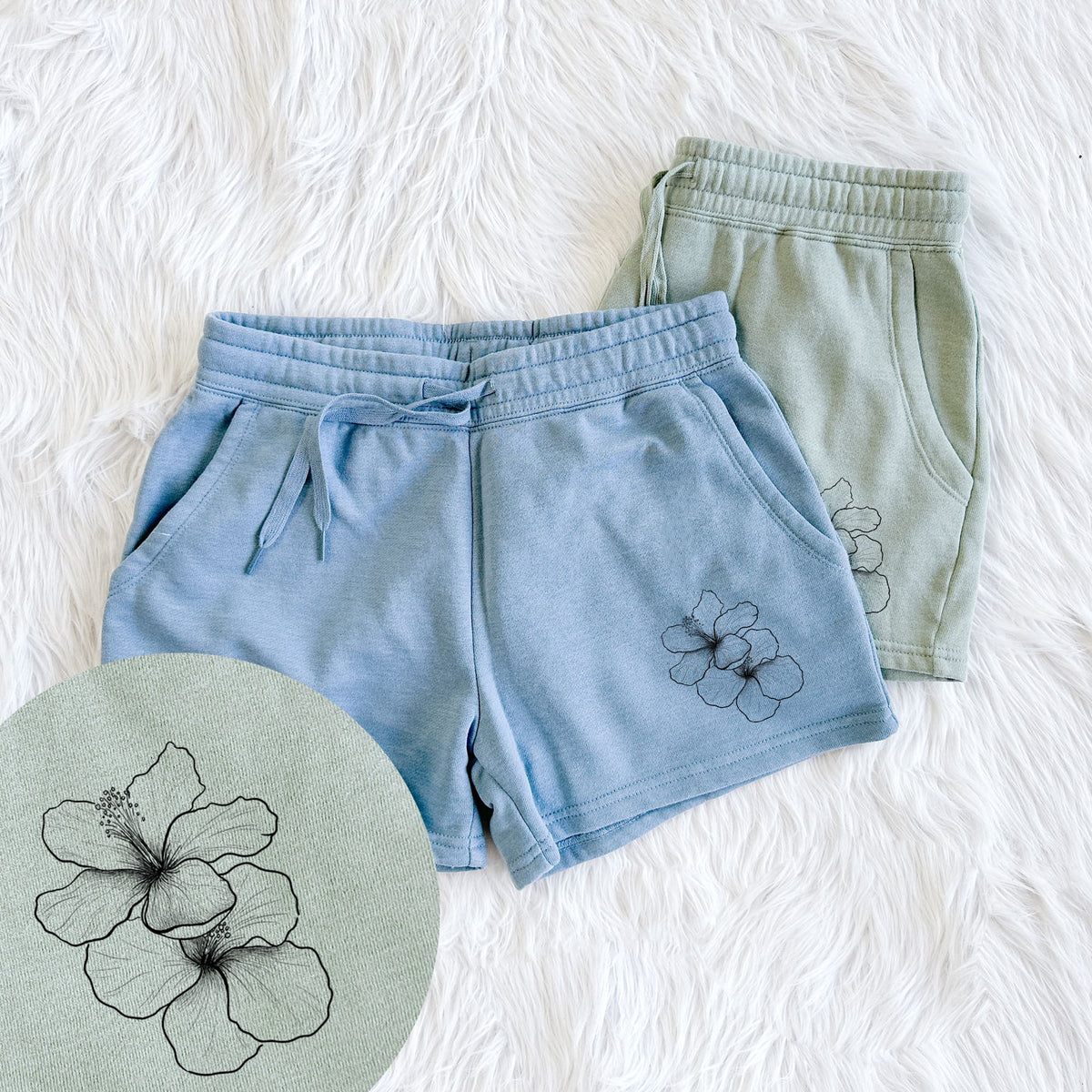 Two pairs of Cali Wave shorts in different colors printed with a black ink line drawing of three hibiscus flowers, with a close-up of the print.