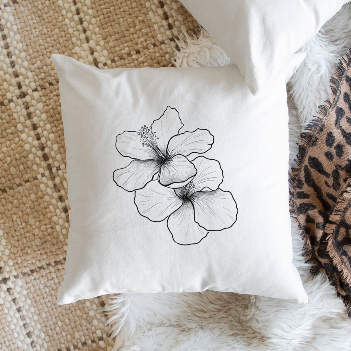 White pillow cover printed with a black ink line drawing of three hibiscus flowers, on a woven chair.