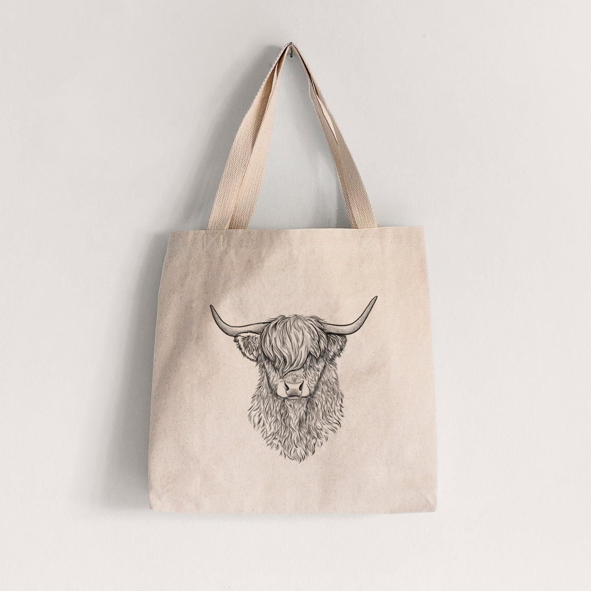 Natural canvas tote bag printed with a detailed black ink portrait of a shaggy highland cow with long curved horns.