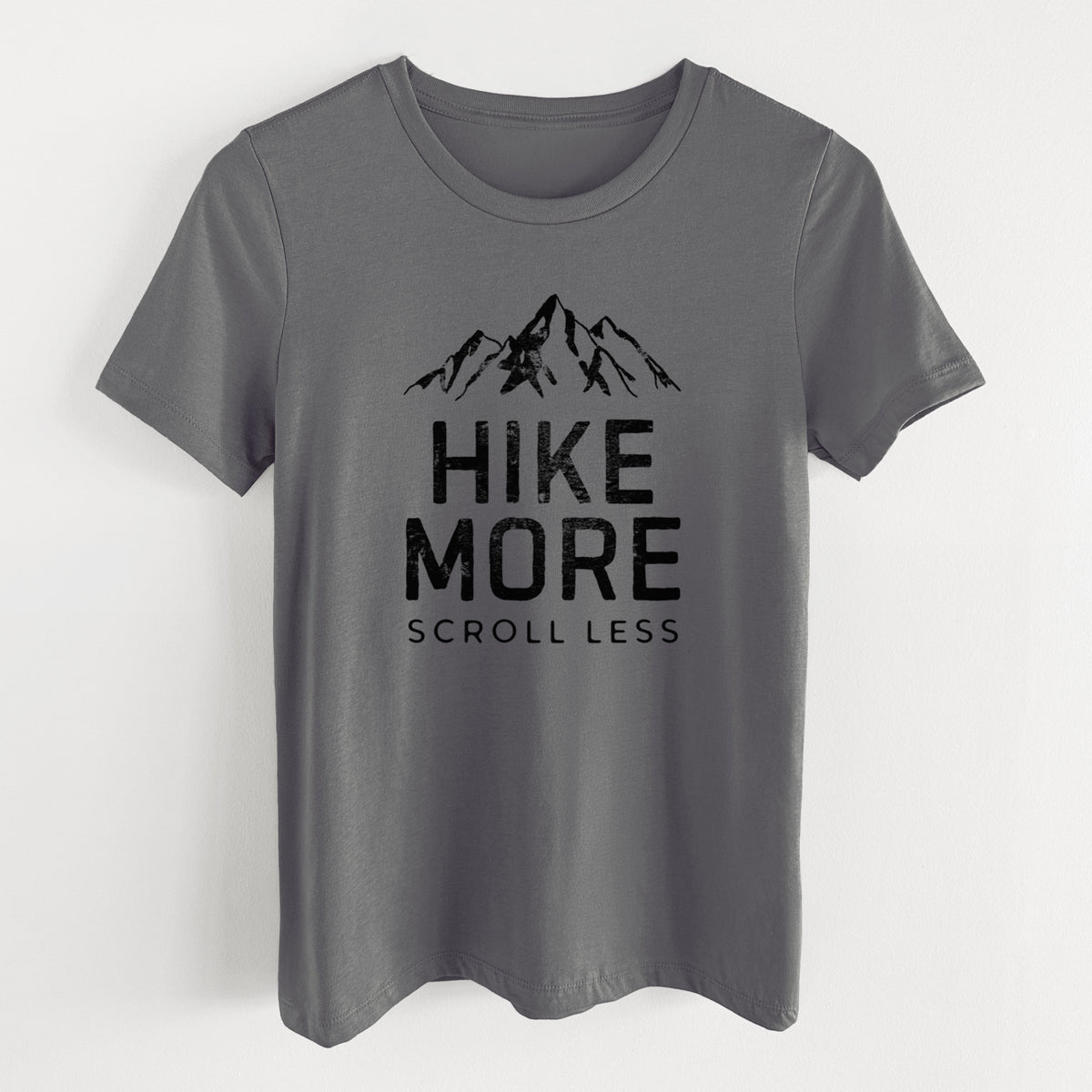 Asphalt women's relaxed fit cotton t-shirt laid flat, printed with black mountain peaks above the bold words Hike More, Scroll Less.