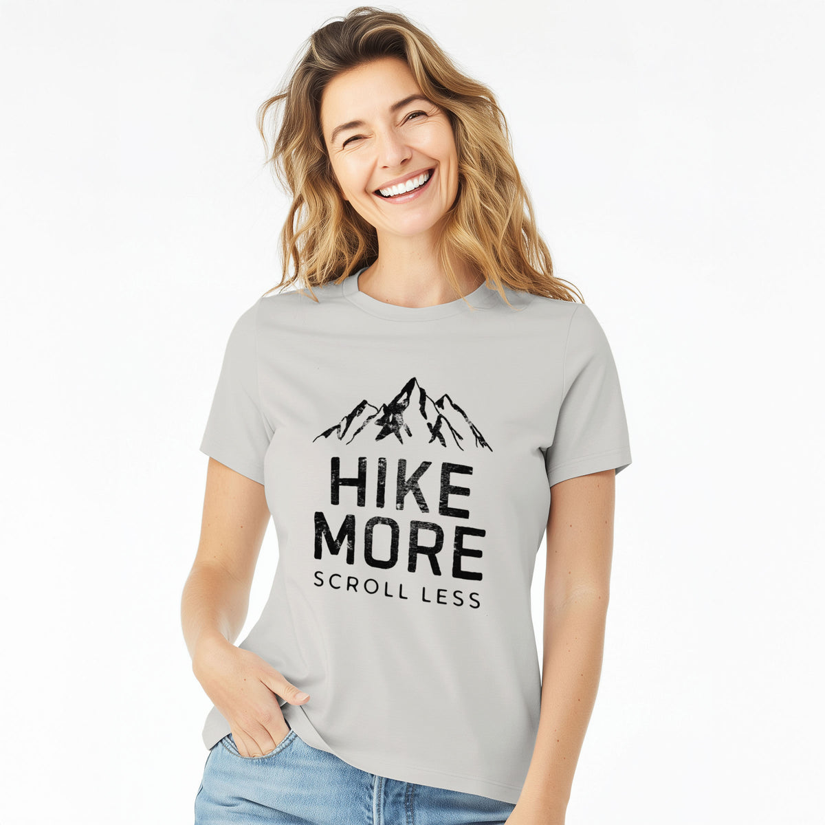 Woman wearing a lunar grey women's relaxed fit cotton t-shirt printed with black mountain peaks above the bold words Hike More, Scroll Less.