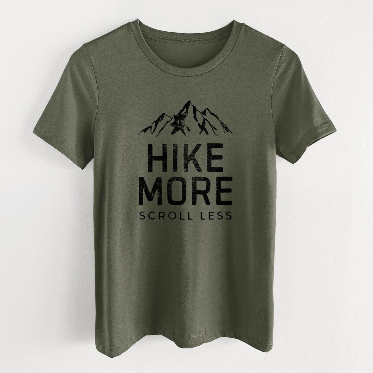 Military green women's relaxed fit cotton t-shirt laid flat, printed with black mountain peaks above the bold words Hike More, Scroll Less.