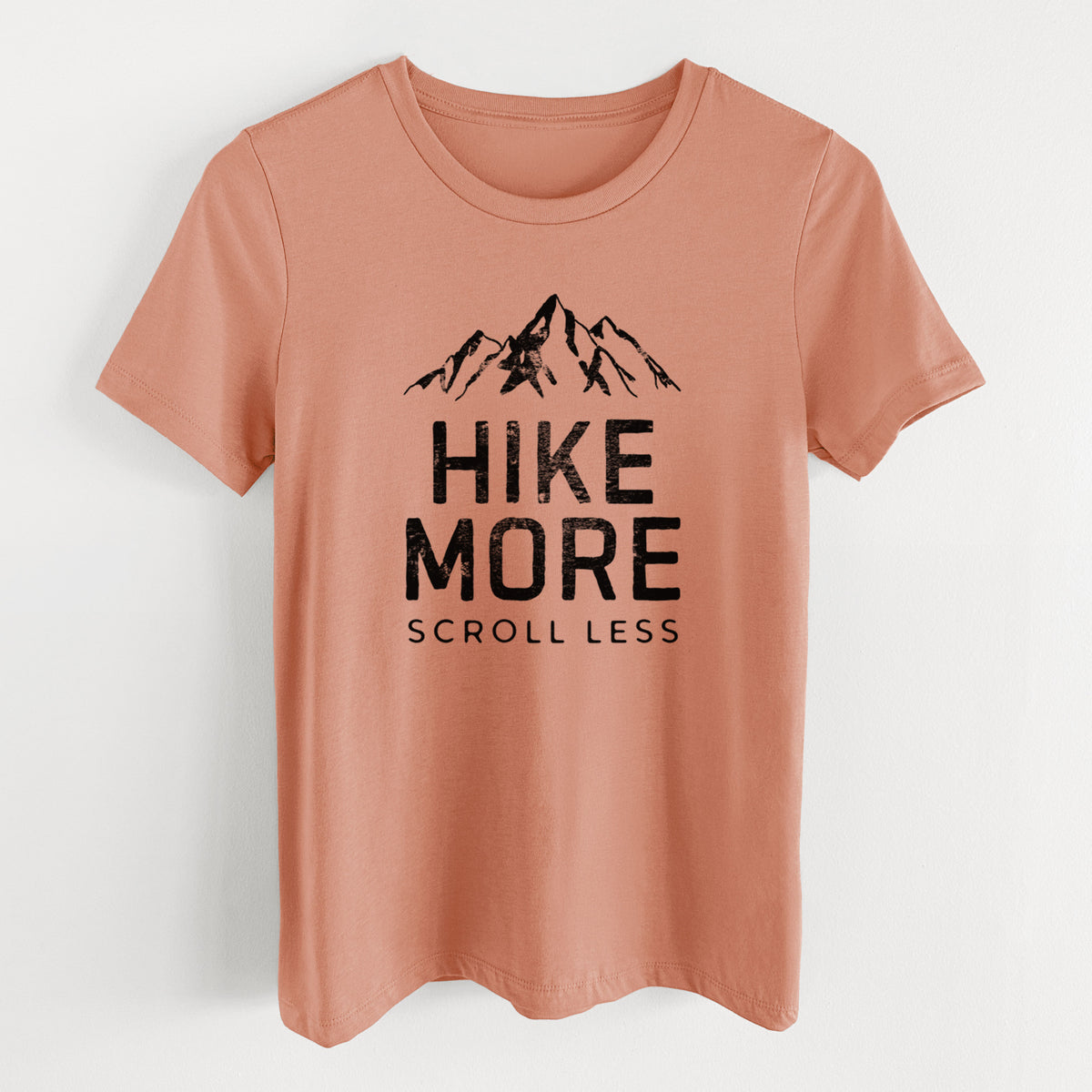 Terracotta orange women's relaxed fit cotton t-shirt laid flat, printed with black mountain peaks above the bold words Hike More, Scroll Less.