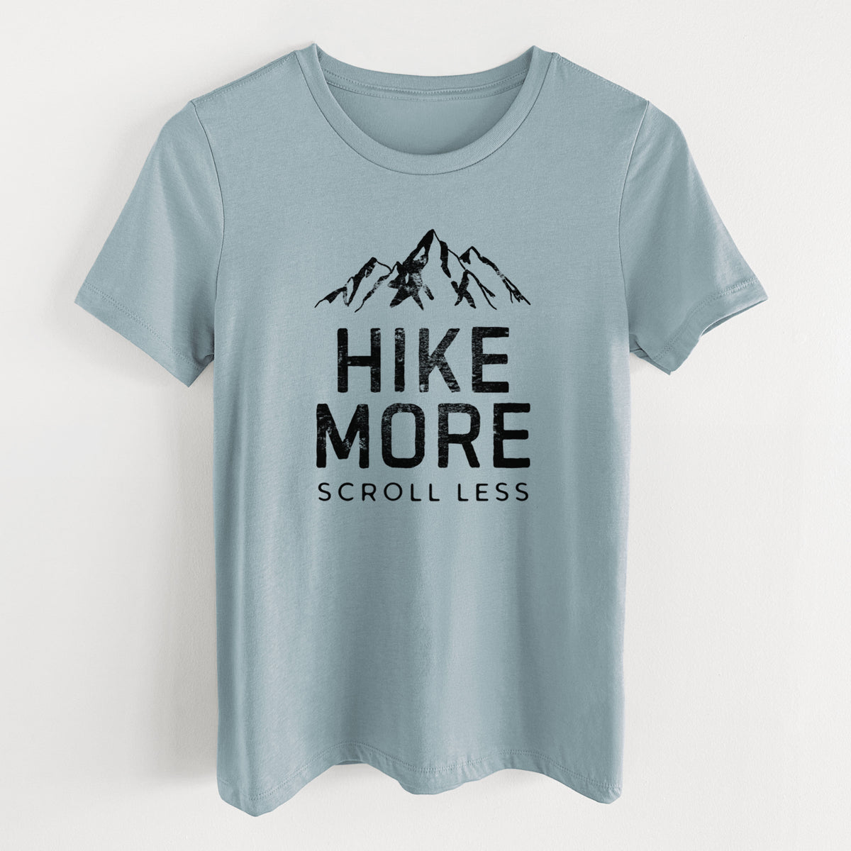 Vintage denim women's relaxed fit cotton t-shirt laid flat, printed with black mountain peaks above the bold words Hike More, Scroll Less.