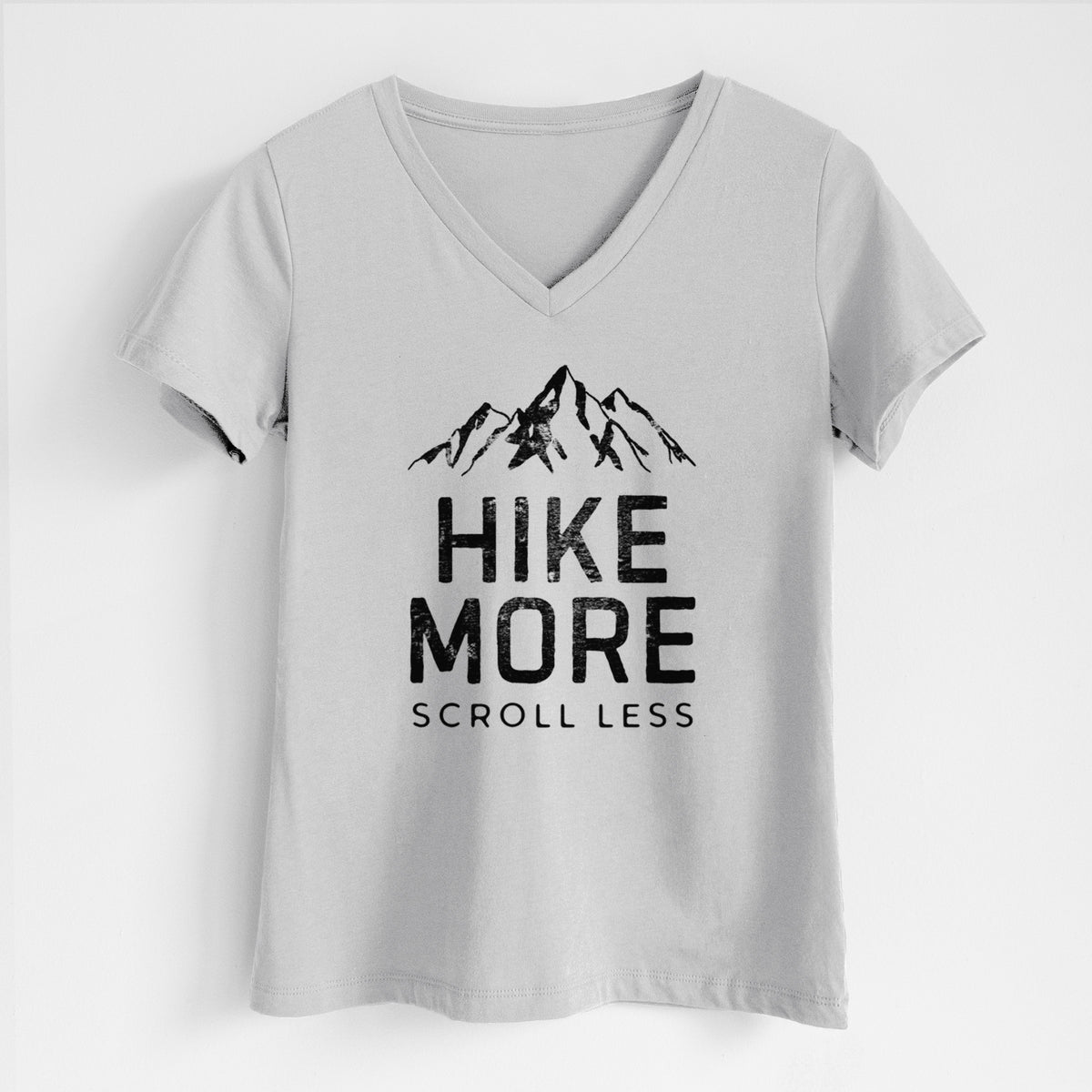 Lunar grey women's relaxed fit cotton V-neck t-shirt laid flat, printed with black mountain peaks above the bold words Hike More, Scroll Less.