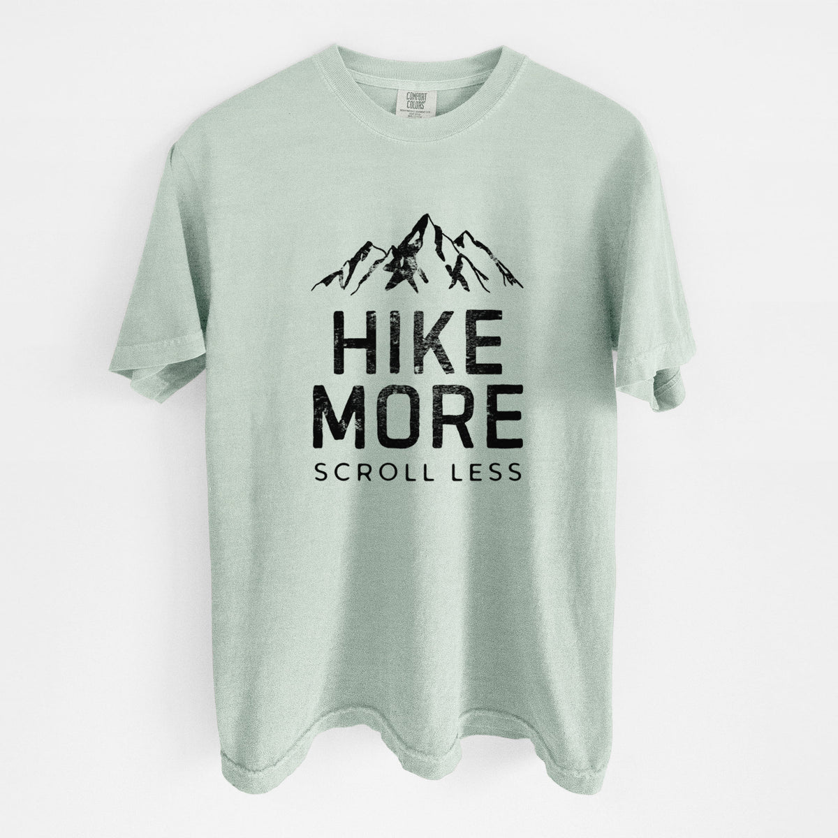 Bay green Comfort Colors t-shirt laid flat, printed with black mountain peaks above the bold words Hike More, Scroll Less.