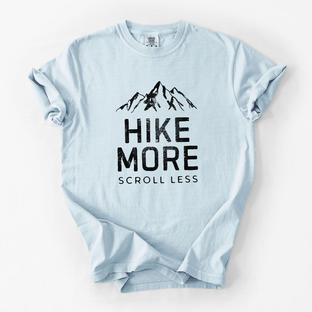 Chambray blue Comfort Colors t-shirt laid flat, printed with black mountain peaks above the bold words Hike More, Scroll Less.