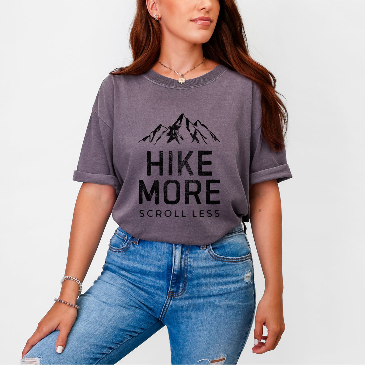 Woman wearing a Comfort Colors t-shirt printed with black mountain peaks above the bold words Hike More, Scroll Less.