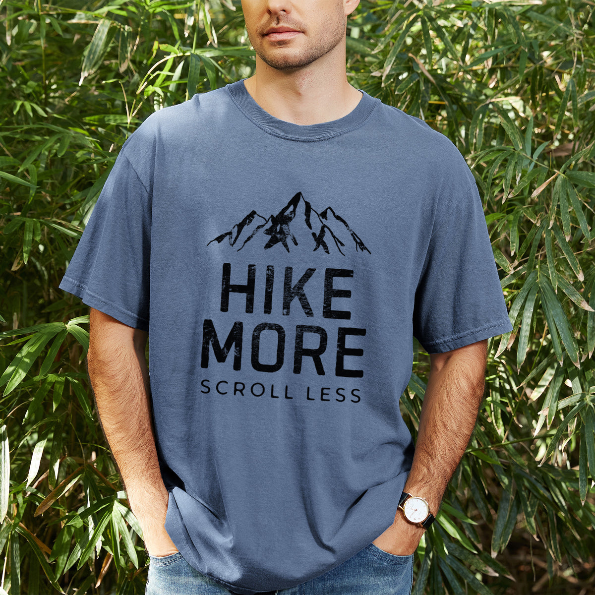 Man wearing a Comfort Colors t-shirt printed with black mountain peaks above the bold words Hike More, Scroll Less, outdoors.