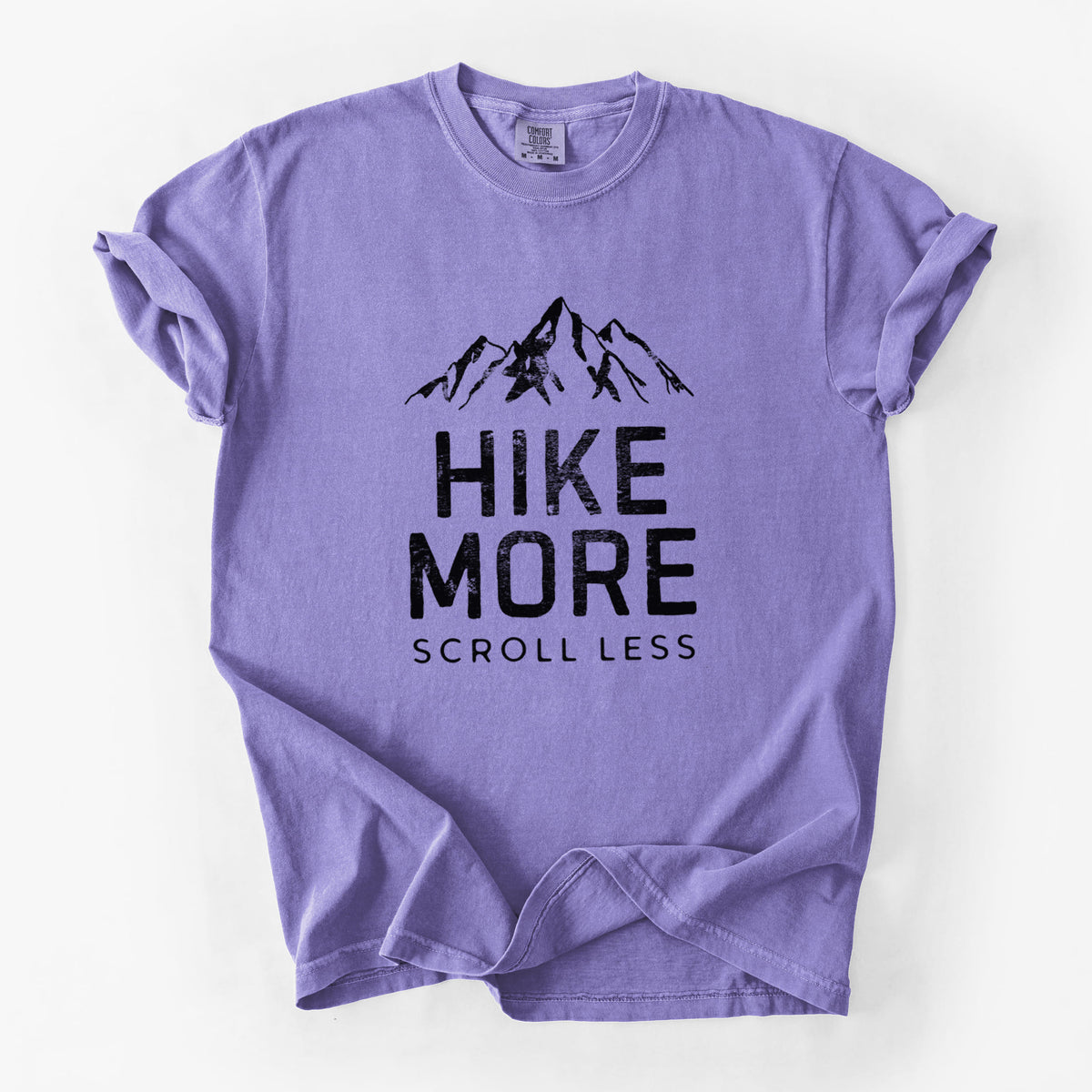Violet purple Comfort Colors t-shirt laid flat, printed with black mountain peaks above the bold words Hike More, Scroll Less.