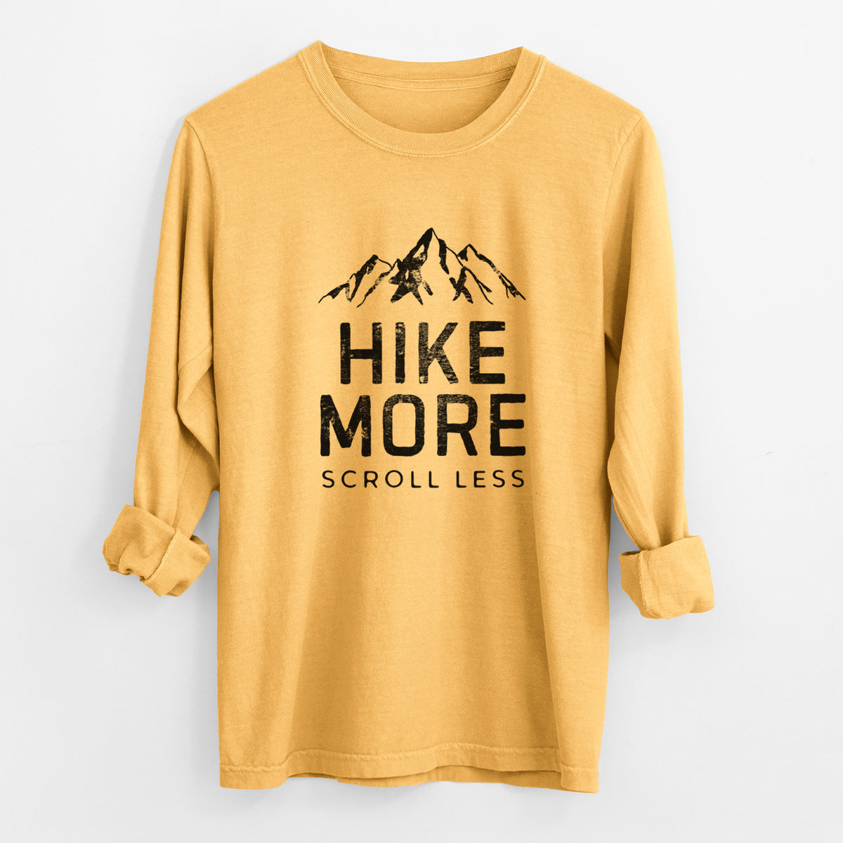 Golden wheat yellow Comfort Colors long sleeve shirt laid flat with the cuffs rolled, printed with black mountain peaks above the bold words Hike More, Scroll Less.