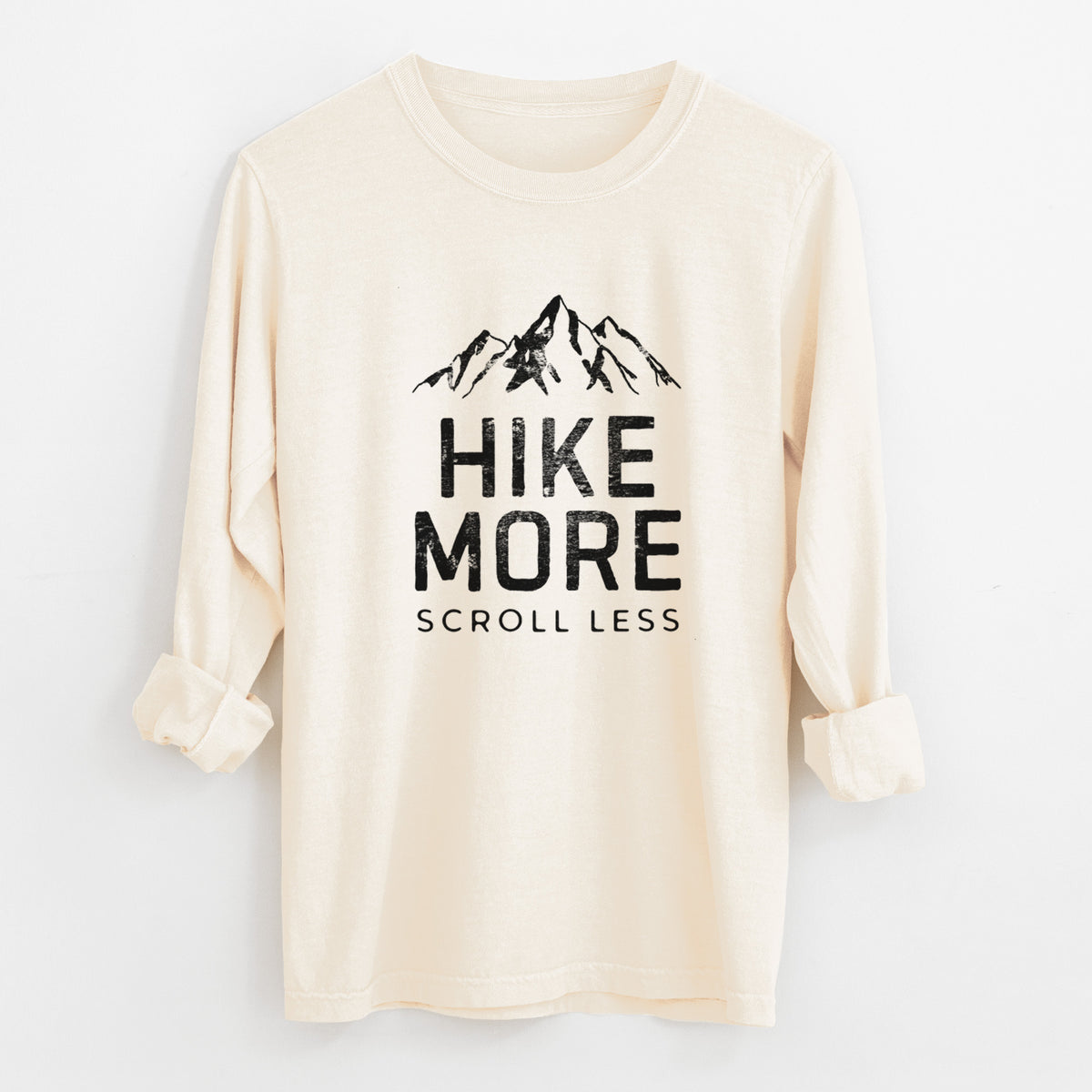 Ivory Comfort Colors long sleeve shirt laid flat with the cuffs rolled, printed with black mountain peaks above the bold words Hike More, Scroll Less.