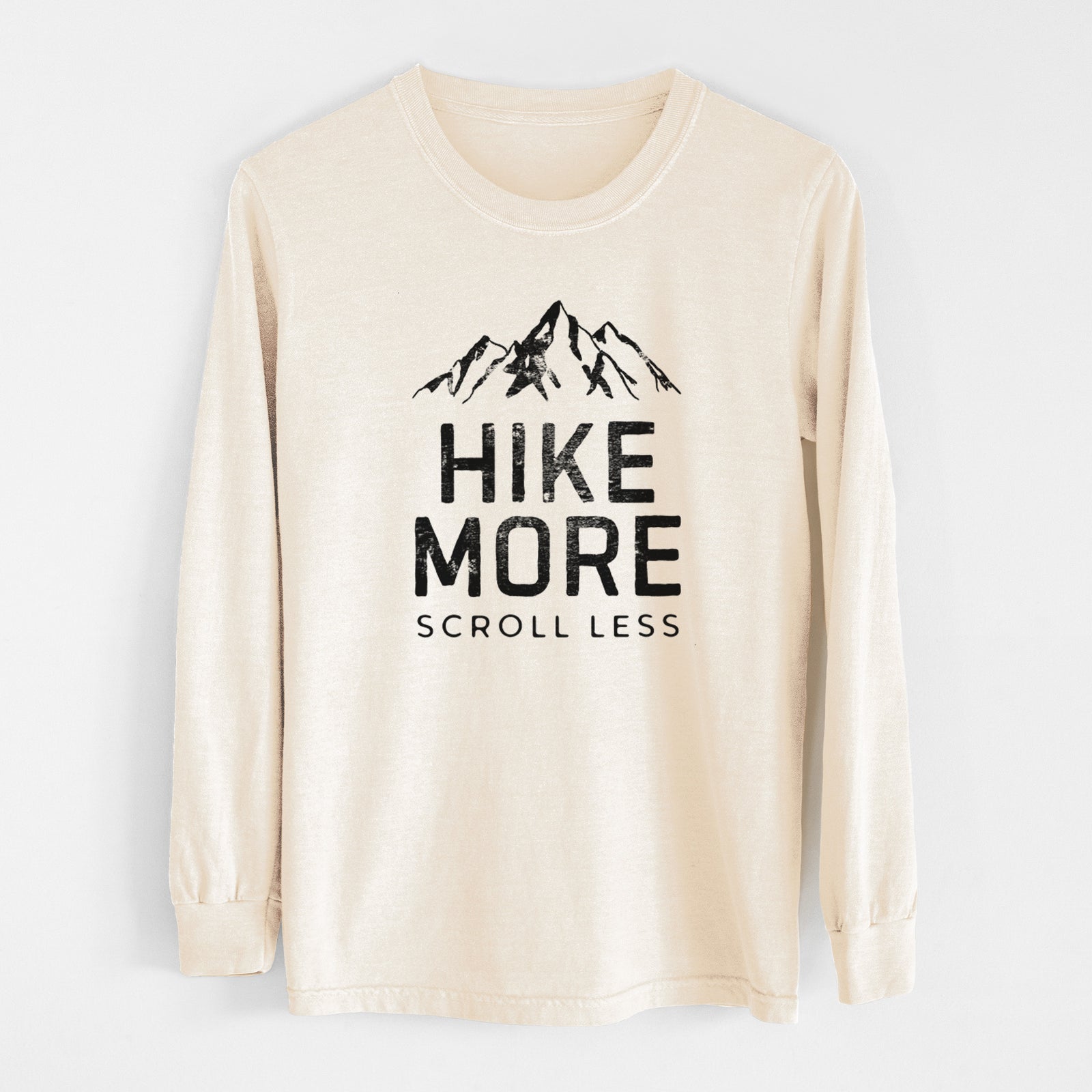 Ivory Comfort Colors long sleeve shirt laid flat, printed with black mountain peaks above the bold words Hike More, Scroll Less.