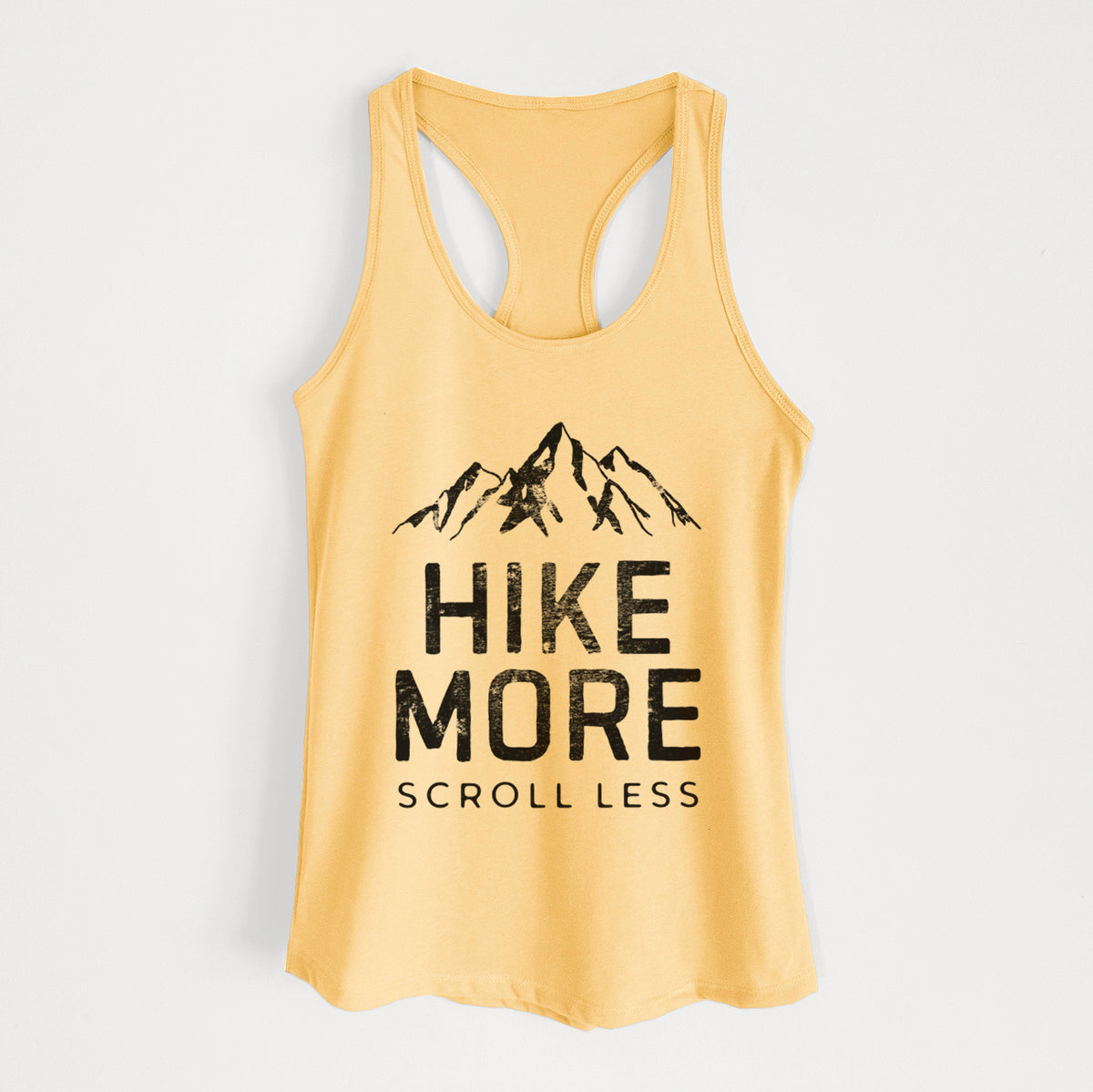 Banana cream women's racerback tank top laid flat, printed with black mountain peaks above the bold words Hike More, Scroll Less.