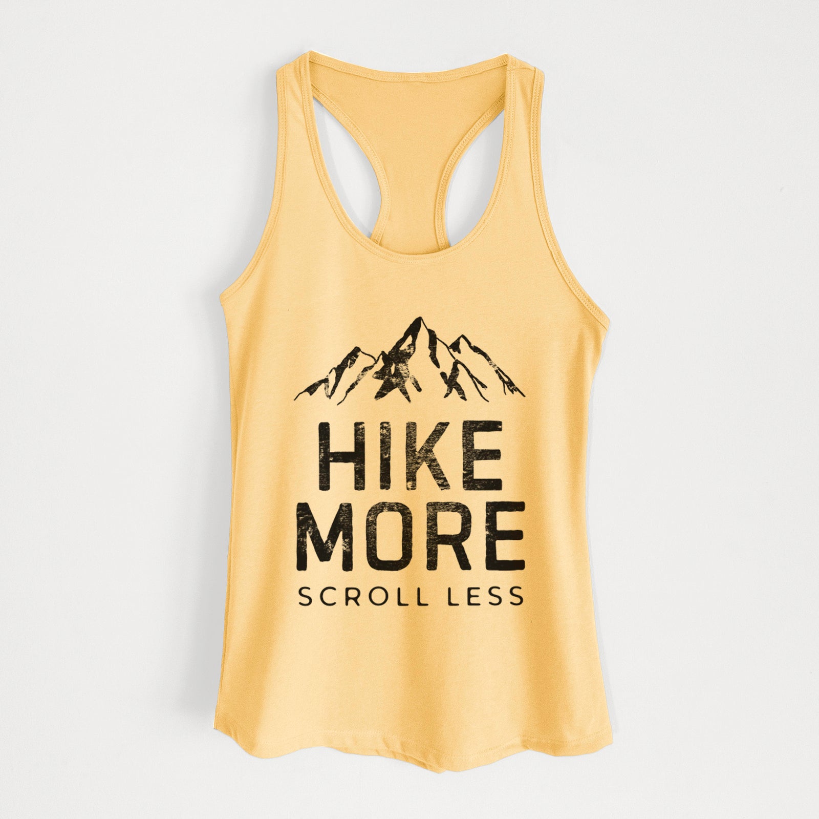Banana cream women's racerback tank top laid flat, printed with black mountain peaks above the bold words Hike More, Scroll Less.