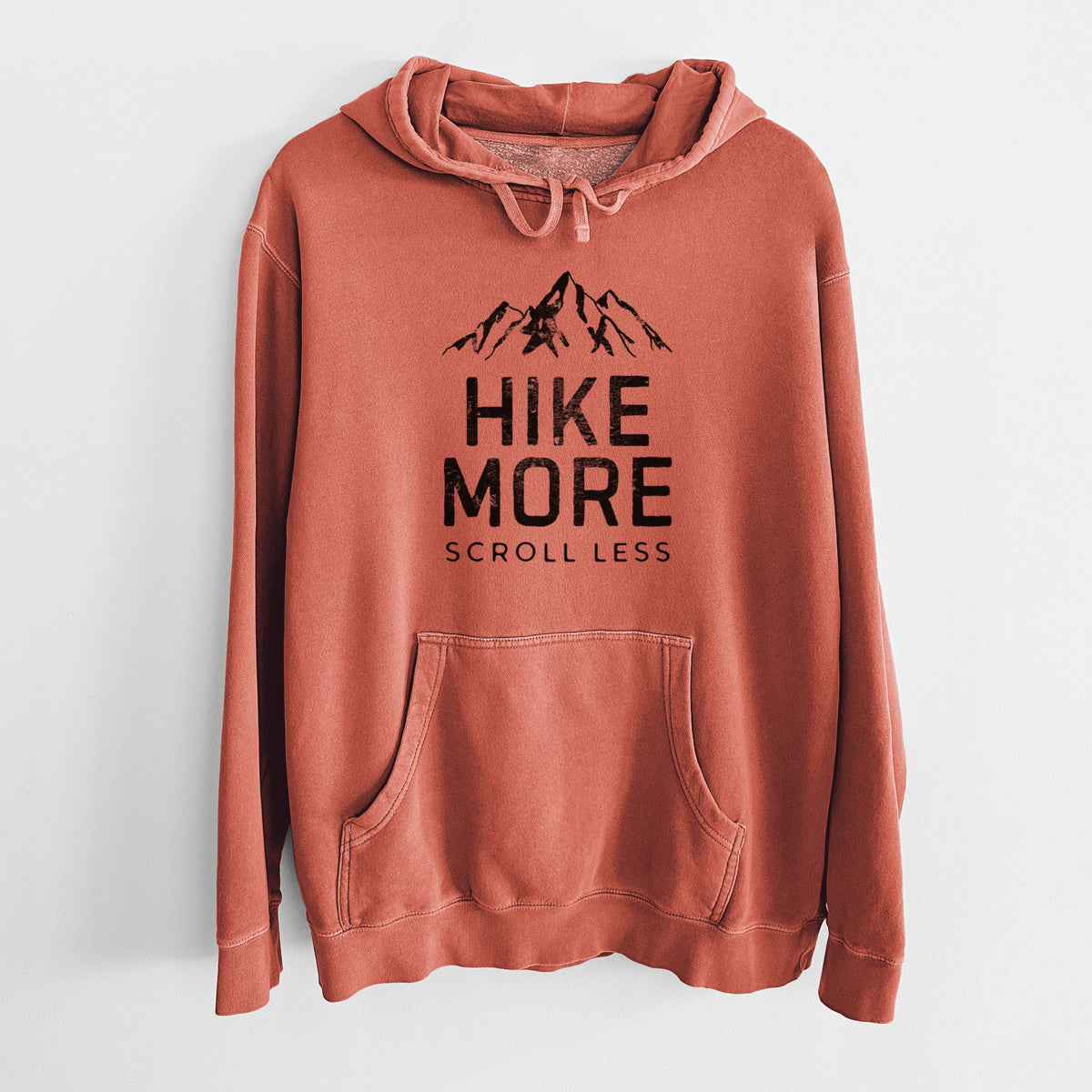 Amber orange pigment dyed hoodie laid flat, printed with black mountain peaks above the bold words Hike More, Scroll Less.