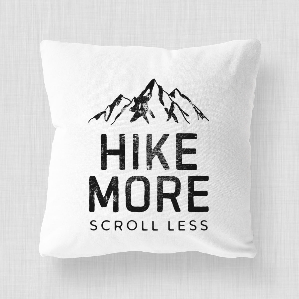 White pillow cover printed with black mountain peaks above the bold words Hike More, Scroll Less.