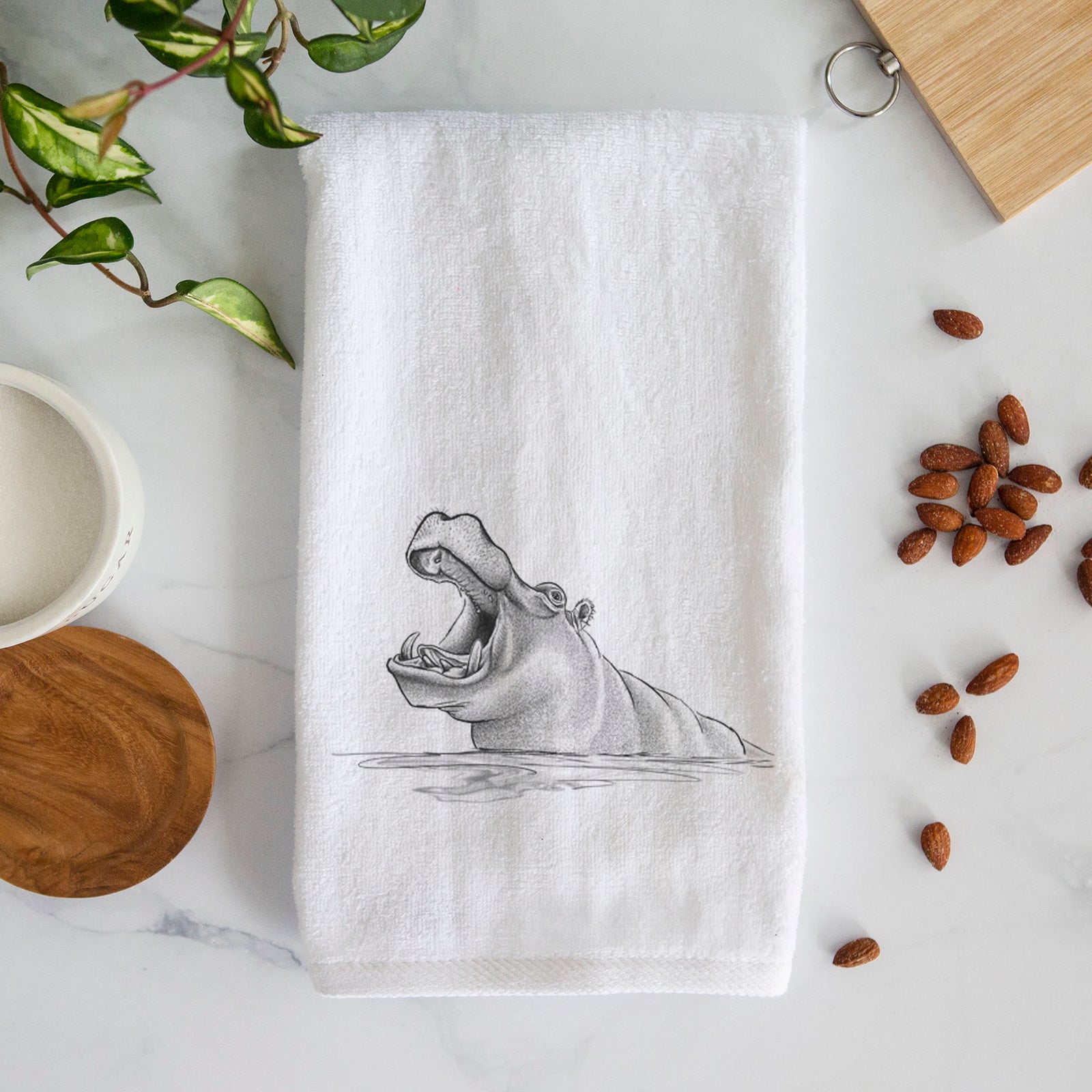 White hand towel printed with a black ink illustration of a hippo yawning with its mouth wide open, half submerged in water.