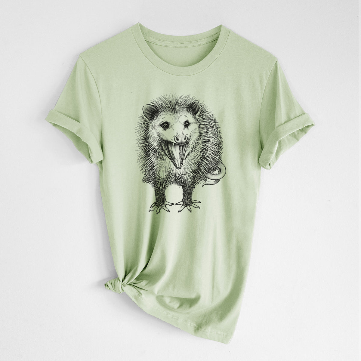 Spring green lightweight cotton t-shirt laid flat with the sleeves rolled, printed with a detailed black ink illustration of an opossum standing and facing forward, mouth open wide in a hiss, with shaggy fur and its tail curled behind.