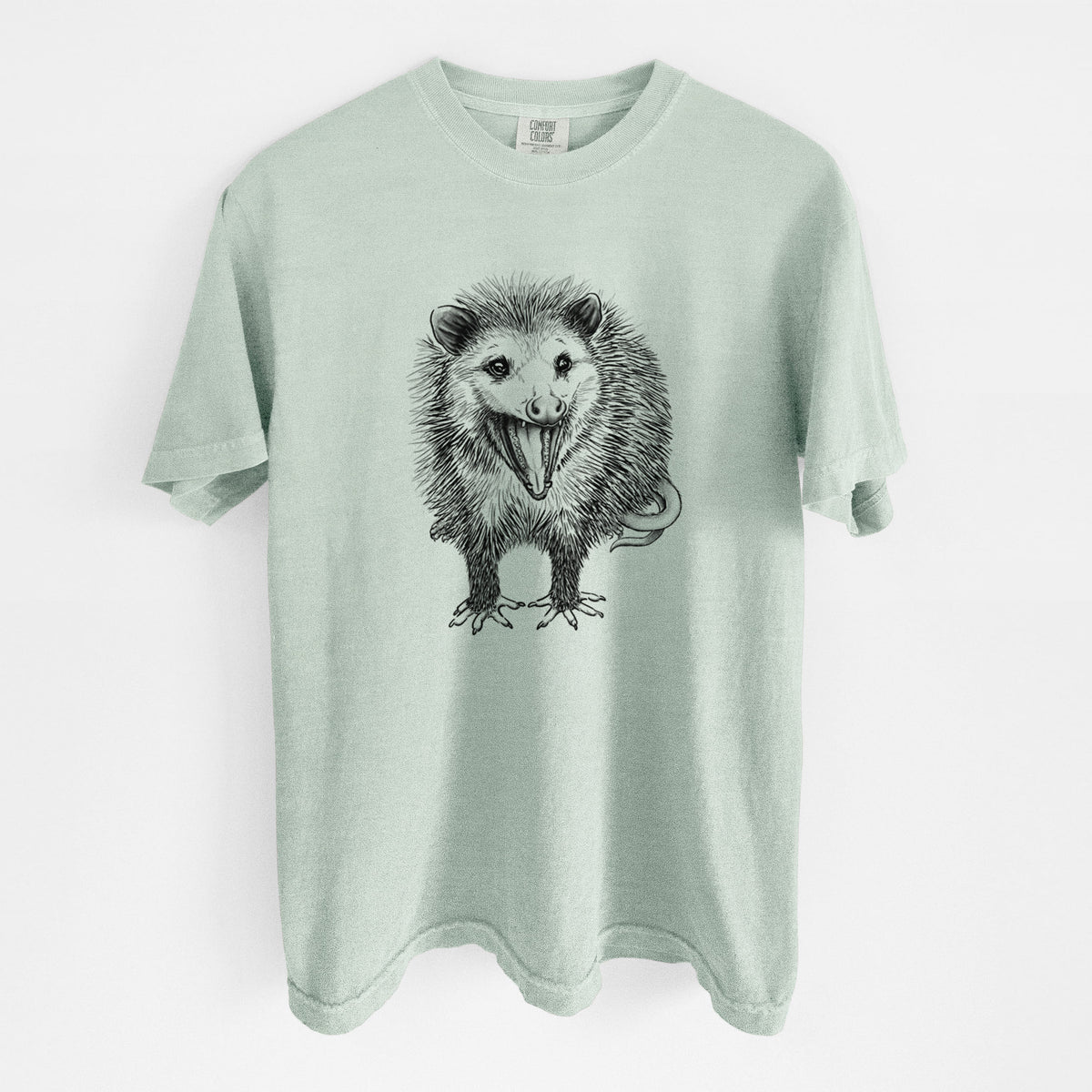 Bay green Comfort Colors t-shirt laid flat, printed with a detailed black ink illustration of an opossum standing and facing forward, mouth open wide in a hiss, with shaggy fur and its tail curled behind.