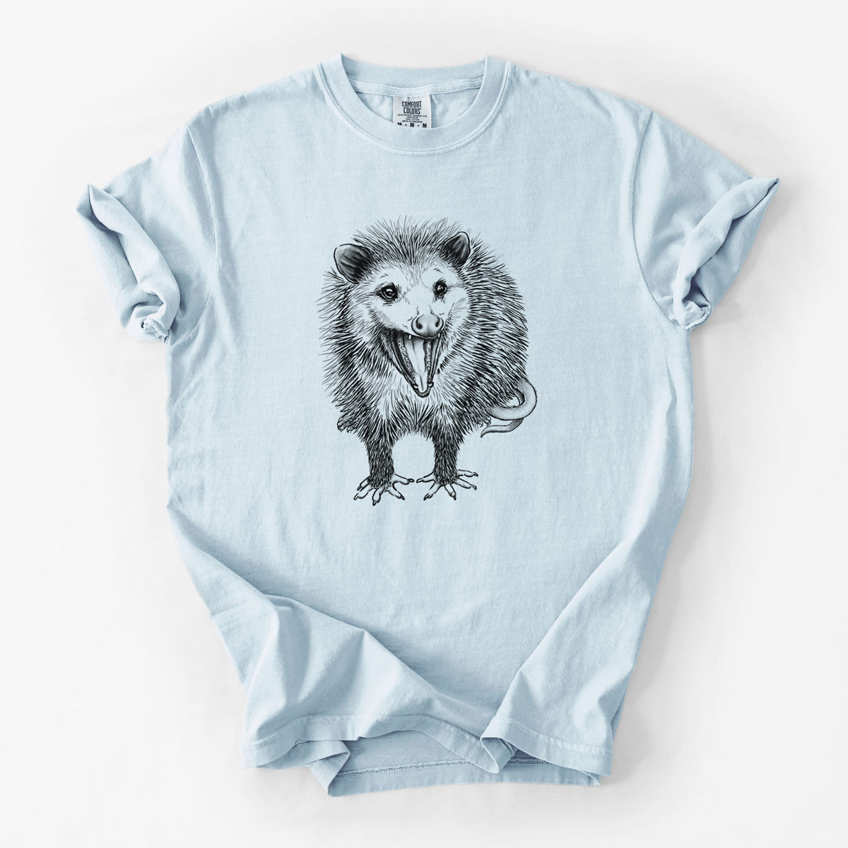 Chambray blue Comfort Colors t-shirt laid flat, printed with a detailed black ink illustration of an opossum standing and facing forward, mouth open wide in a hiss, with shaggy fur and its tail curled behind.
