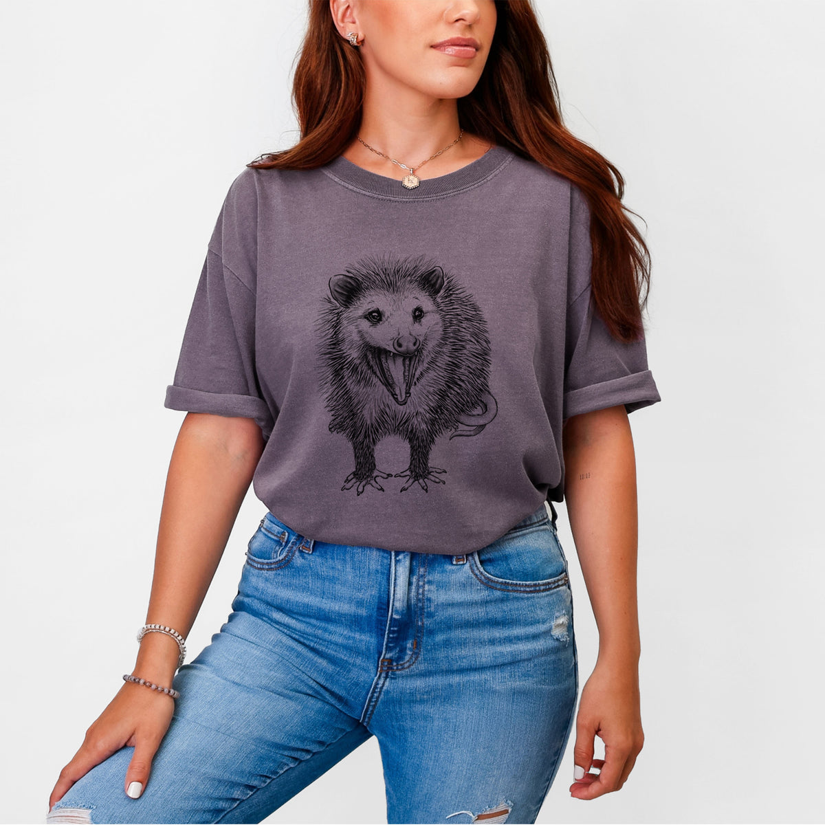 Woman wearing a Comfort Colors t-shirt printed with a detailed black ink illustration of an opossum standing and facing forward, mouth open wide in a hiss, with shaggy fur and its tail curled behind.