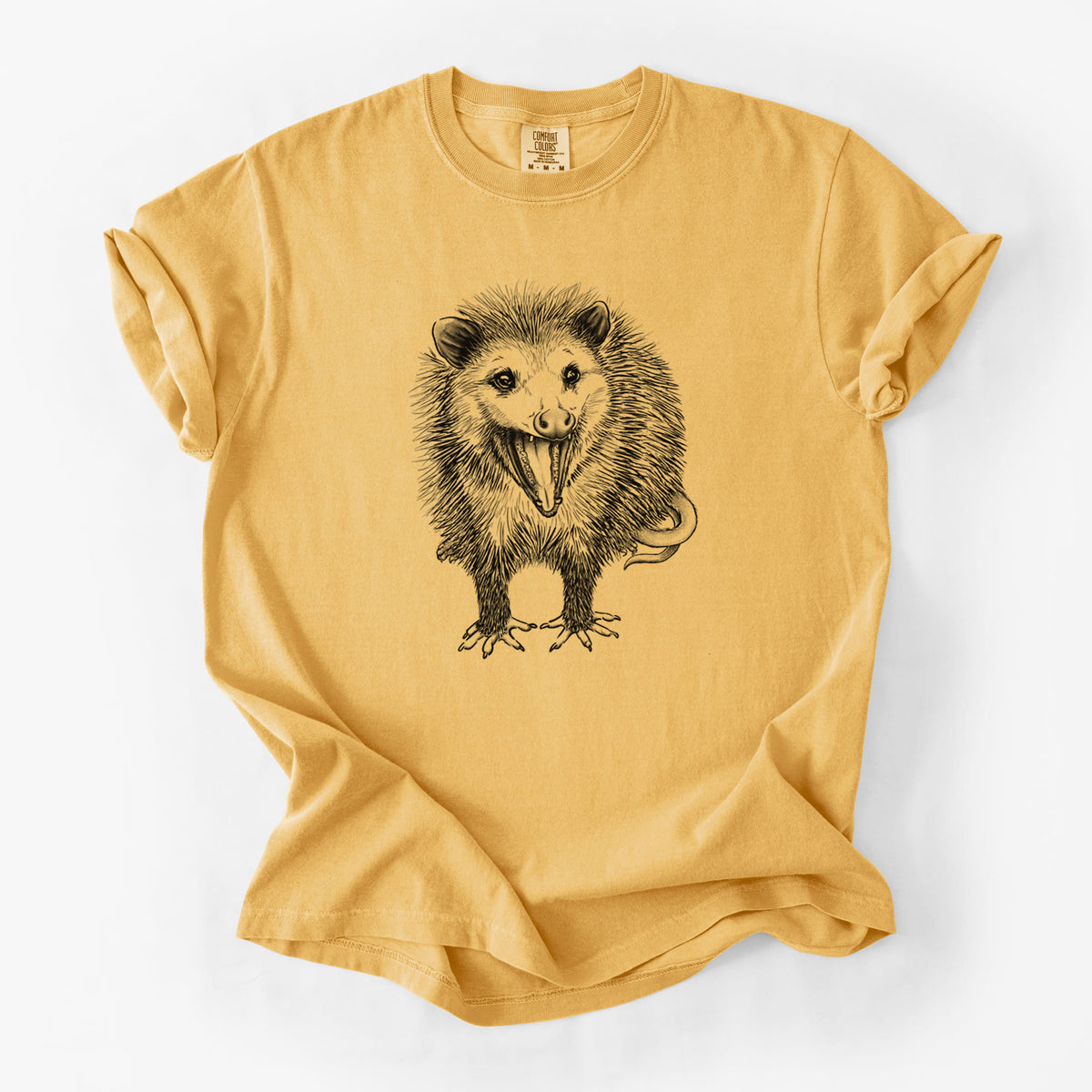 Golden wheat yellow Comfort Colors t-shirt laid flat, printed with a detailed black ink illustration of an opossum standing and facing forward, mouth open wide in a hiss, with shaggy fur and its tail curled behind.
