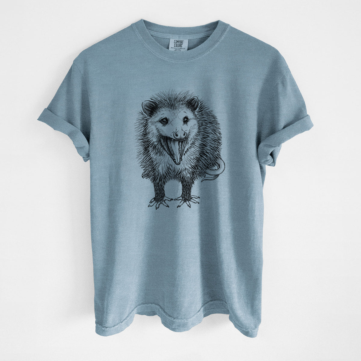 Steel blue Comfort Colors t-shirt laid flat, printed with a detailed black ink illustration of an opossum standing and facing forward, mouth open wide in a hiss, with shaggy fur and its tail curled behind.