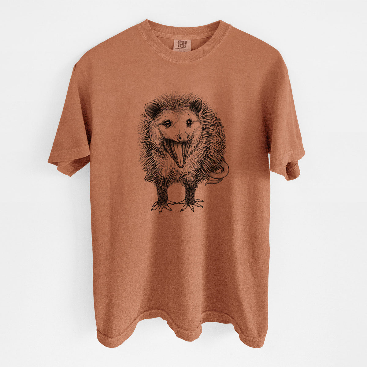 Yam burnt orange Comfort Colors t-shirt laid flat, printed with a detailed black ink illustration of an opossum standing and facing forward, mouth open wide in a hiss, with shaggy fur and its tail curled behind.