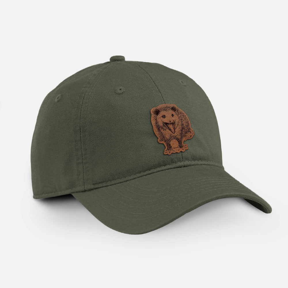 Olive cotton baseball hat with a detailed black ink illustration of an opossum standing and facing forward, mouth open wide in a hiss, with shaggy fur and its tail curled behind on the front.