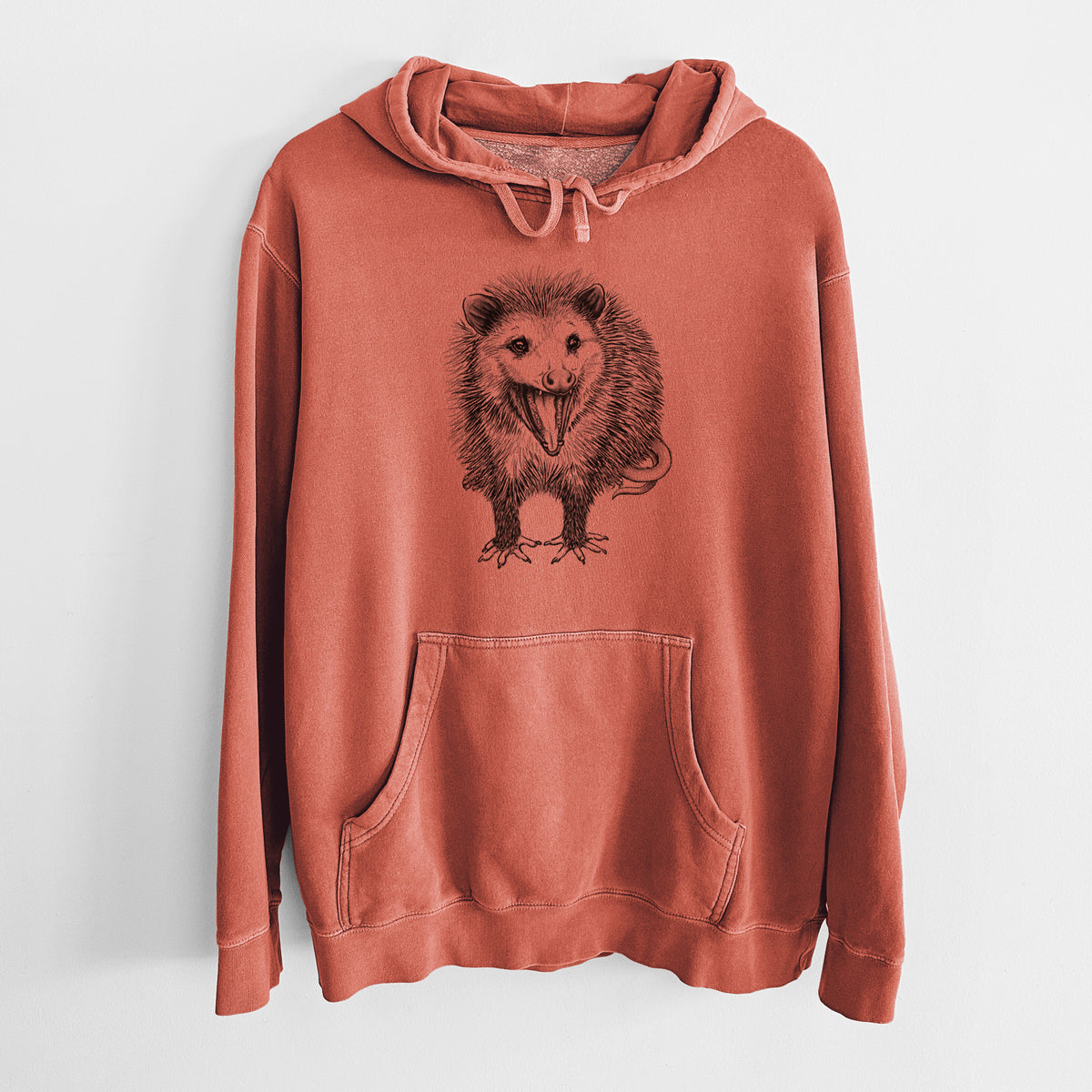 Amber orange pigment dyed hoodie laid flat, printed with a detailed black ink illustration of an opossum standing and facing forward, mouth open wide in a hiss, with shaggy fur and its tail curled behind.