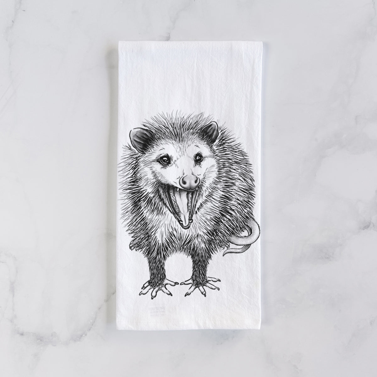 White cotton tea towel laid flat on marble, printed with a detailed black ink illustration of an opossum standing and facing forward, mouth open wide in a hiss, with shaggy fur and its tail curled behind.