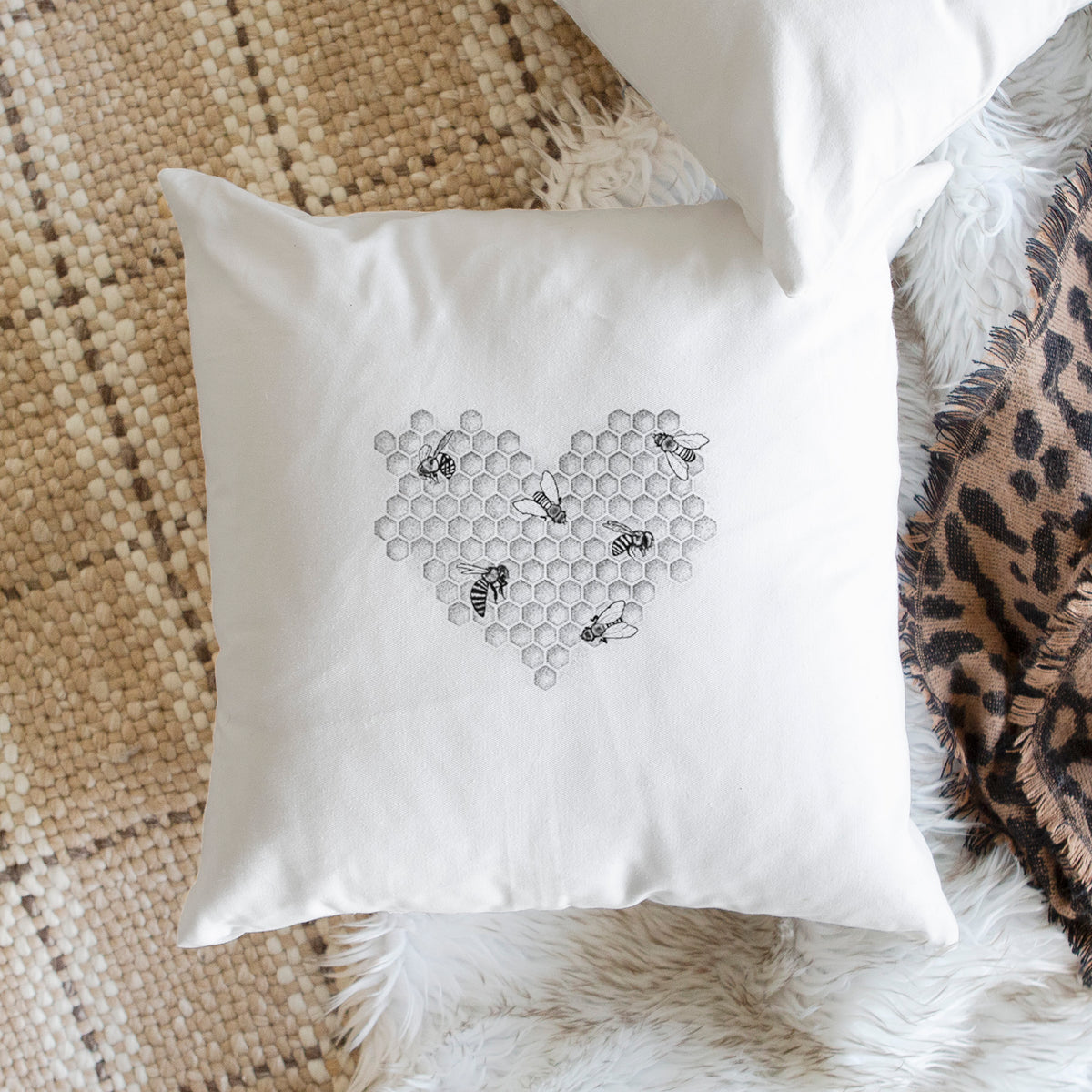 White pillow cover printed with a black ink heart made of honeycomb cells with small bees crawling across it, on a woven chair.