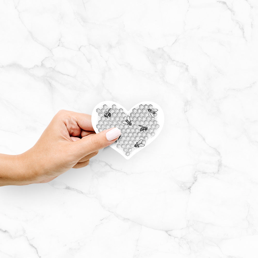 Hand holding a 4 inch vinyl decal of a black ink heart made of honeycomb cells with small bees crawling across it.