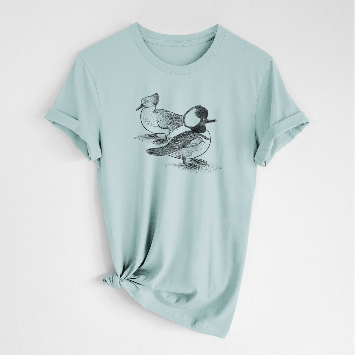 Dusty blue lightweight cotton t-shirt laid flat with the sleeves rolled, printed with a detailed black ink illustration of a pair of hooded mergansers, male and female.