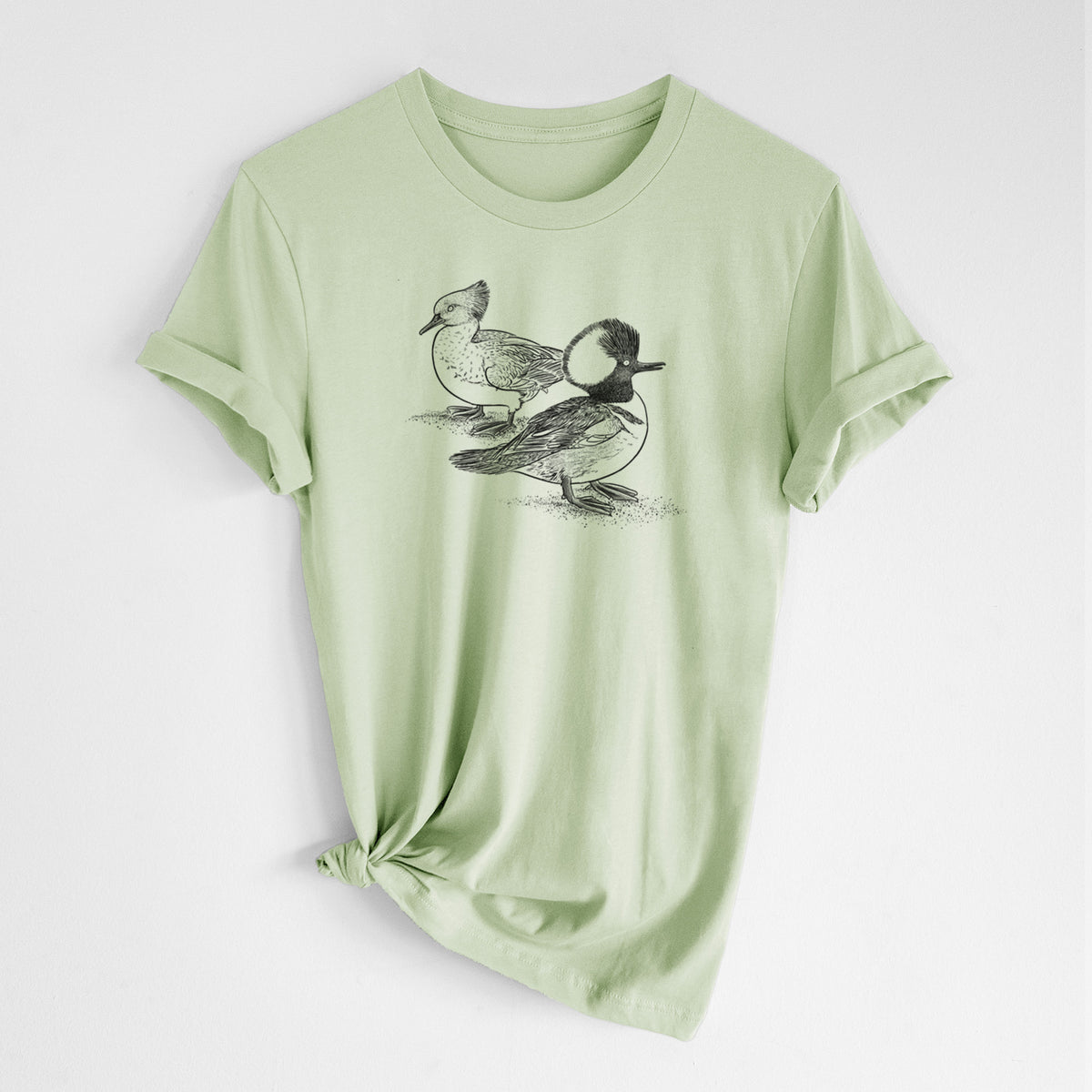 Spring green lightweight cotton t-shirt laid flat with the sleeves rolled, printed with a detailed black ink illustration of a pair of hooded mergansers, male and female.