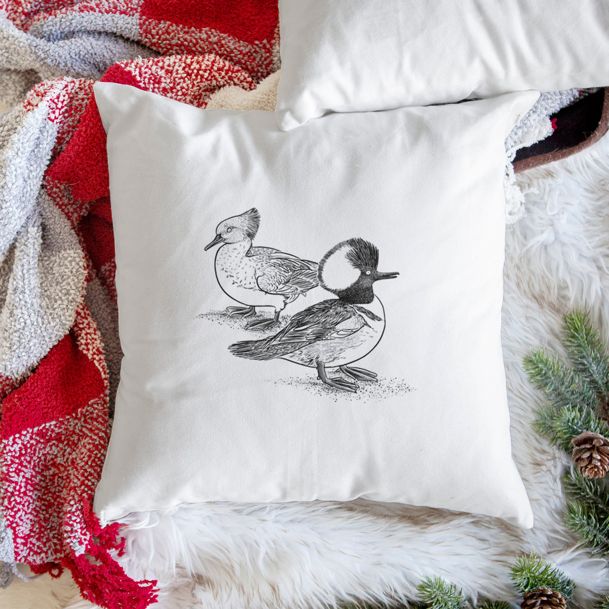 White pillow cover printed with a detailed black ink illustration of a pair of hooded mergansers, male and female, on a woven chair.