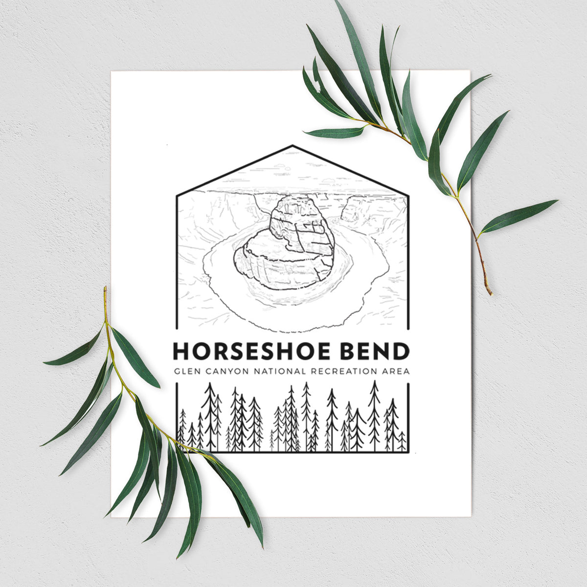 Art print of a black line art badge of Horseshoe Bend above pine trees, with the words Horseshoe Bend, shown with eucalyptus leaves.