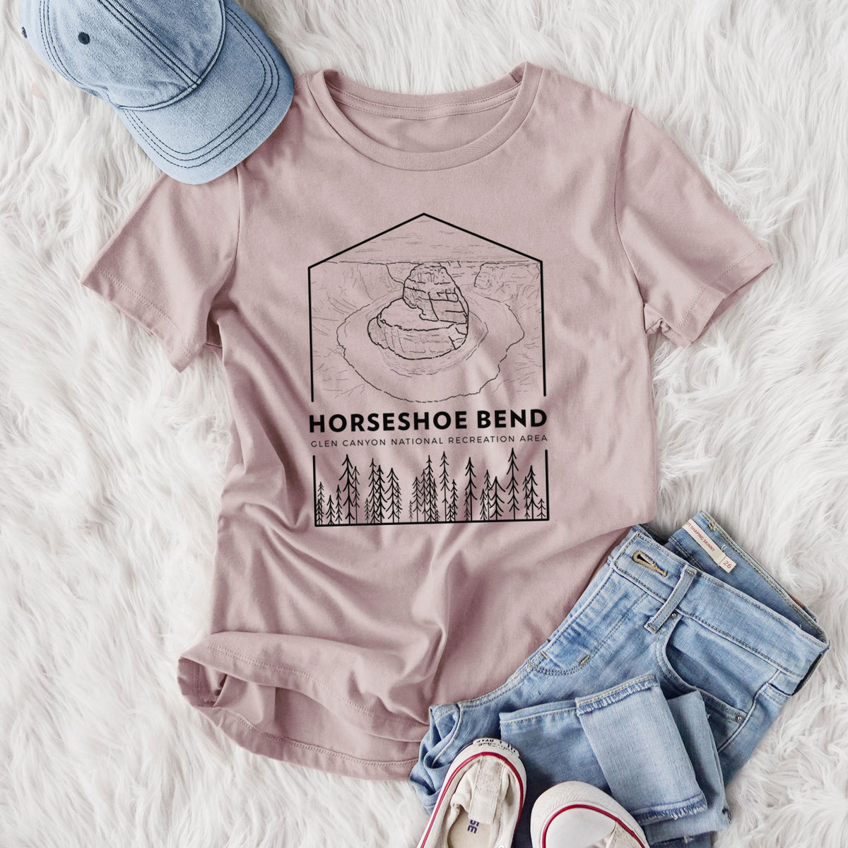 Women's relaxed fit cotton t-shirt printed with a black line art badge of Horseshoe Bend above pine trees, with the words Horseshoe Bend, styled flat on a white faux fur rug with jeans.