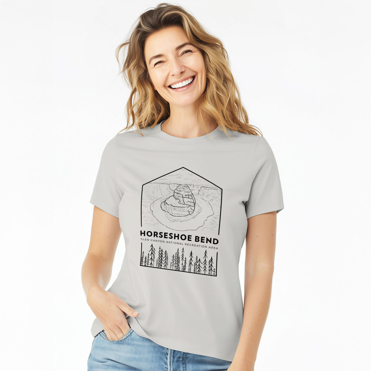 Woman wearing a lunar grey women's relaxed fit cotton t-shirt printed with a black line art badge of Horseshoe Bend above pine trees, with the words Horseshoe Bend.