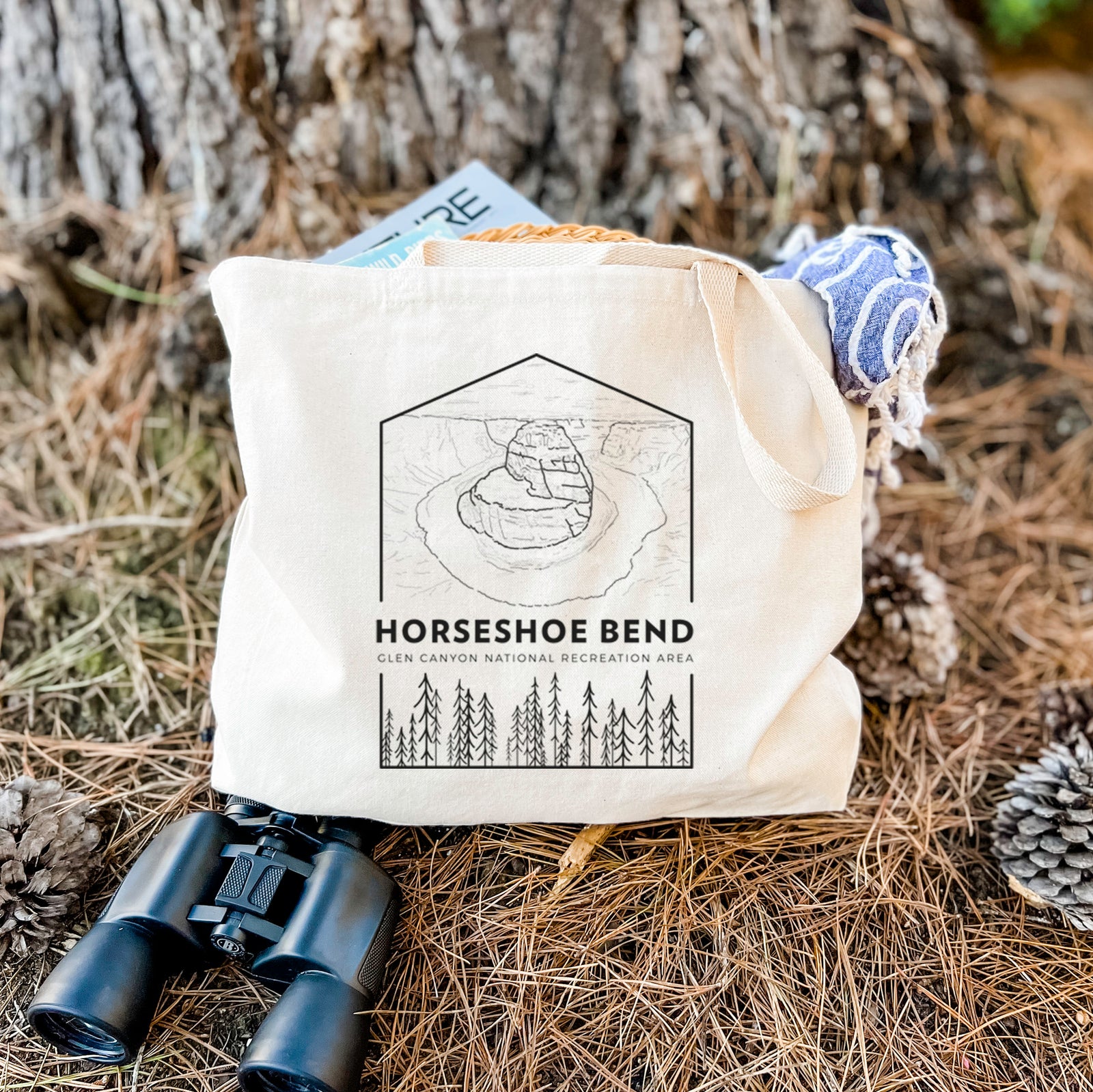 Natural canvas tote bag printed with a black line art badge of Horseshoe Bend above pine trees, with the words Horseshoe Bend.
