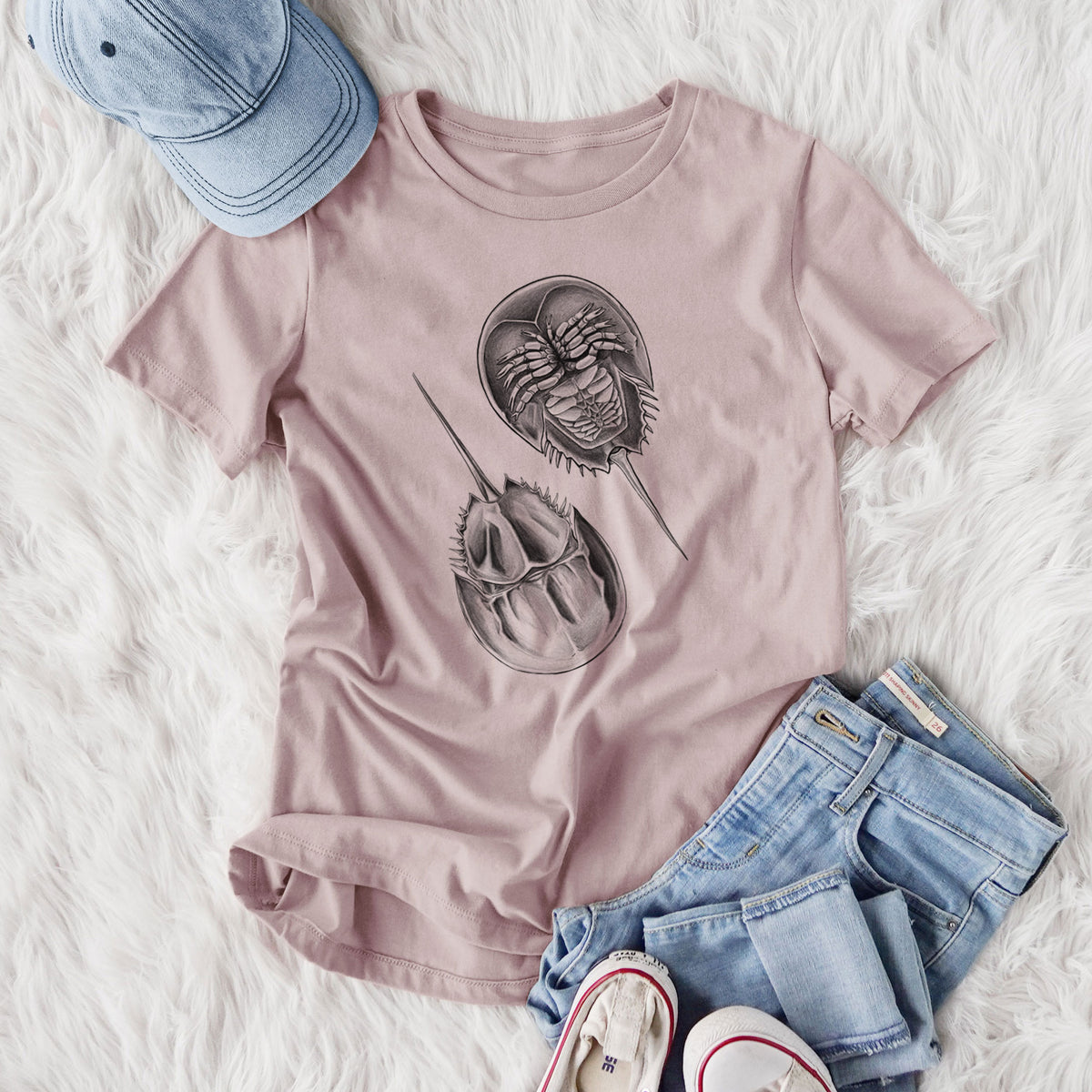 Women's relaxed fit cotton t-shirt printed with a detailed black ink illustration of two horseshoe crabs, styled flat on a white faux fur rug with jeans.