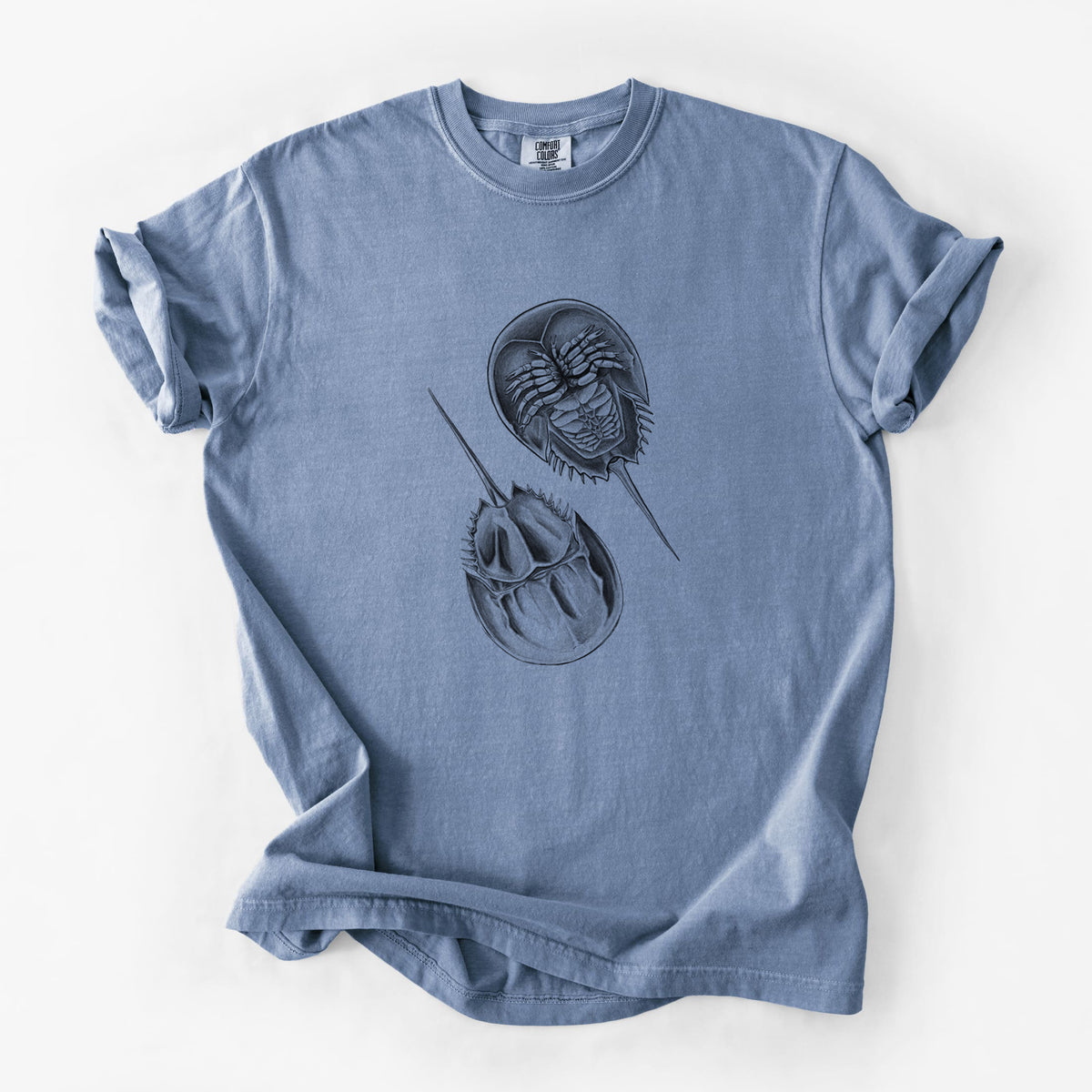 Blue jean Comfort Colors t-shirt laid flat, printed with a detailed black ink illustration of two horseshoe crabs.