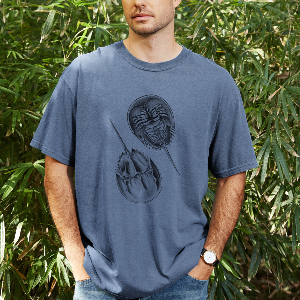 Man wearing a Comfort Colors t-shirt printed with a detailed black ink illustration of two horseshoe crabs, outdoors.
