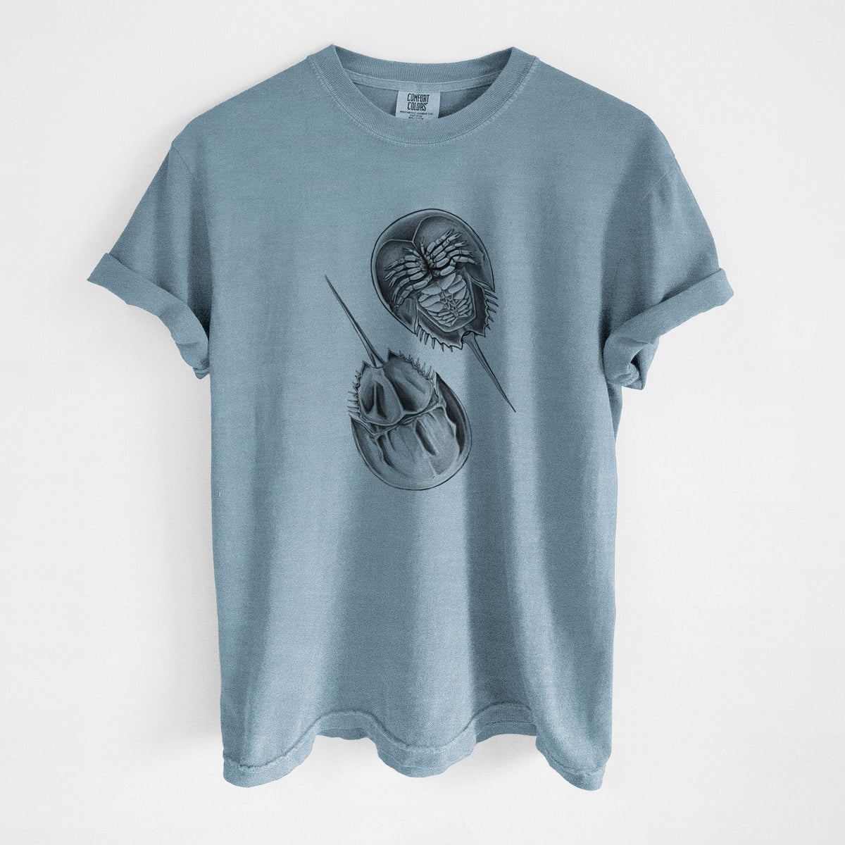 Steel blue Comfort Colors t-shirt laid flat, printed with a detailed black ink illustration of two horseshoe crabs.